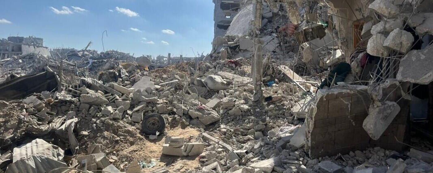 Sönderbombade byggnader och stora mängder bråte i ett bostadsområde i Gaza, med blå himmel i bakgrunden.