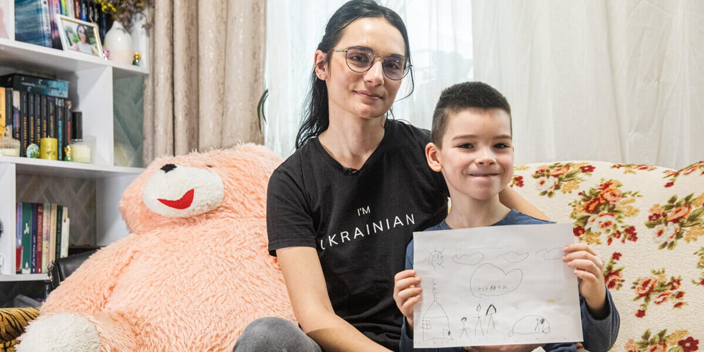 En kvinna och en pojke sitter tätt intill varandra i en soffa i ett vardagsrum. Kvinnan har armen om pojken och ser lugnt in i kameran.