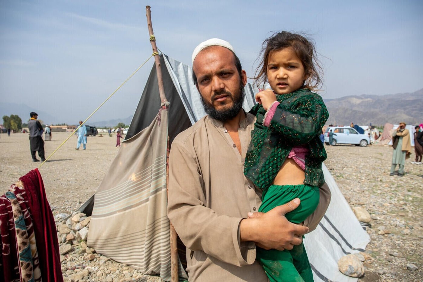 En man håller sin dotter utanför ett provisoriskt tält i ett läger för internflyktingar i östra Afghanistan.