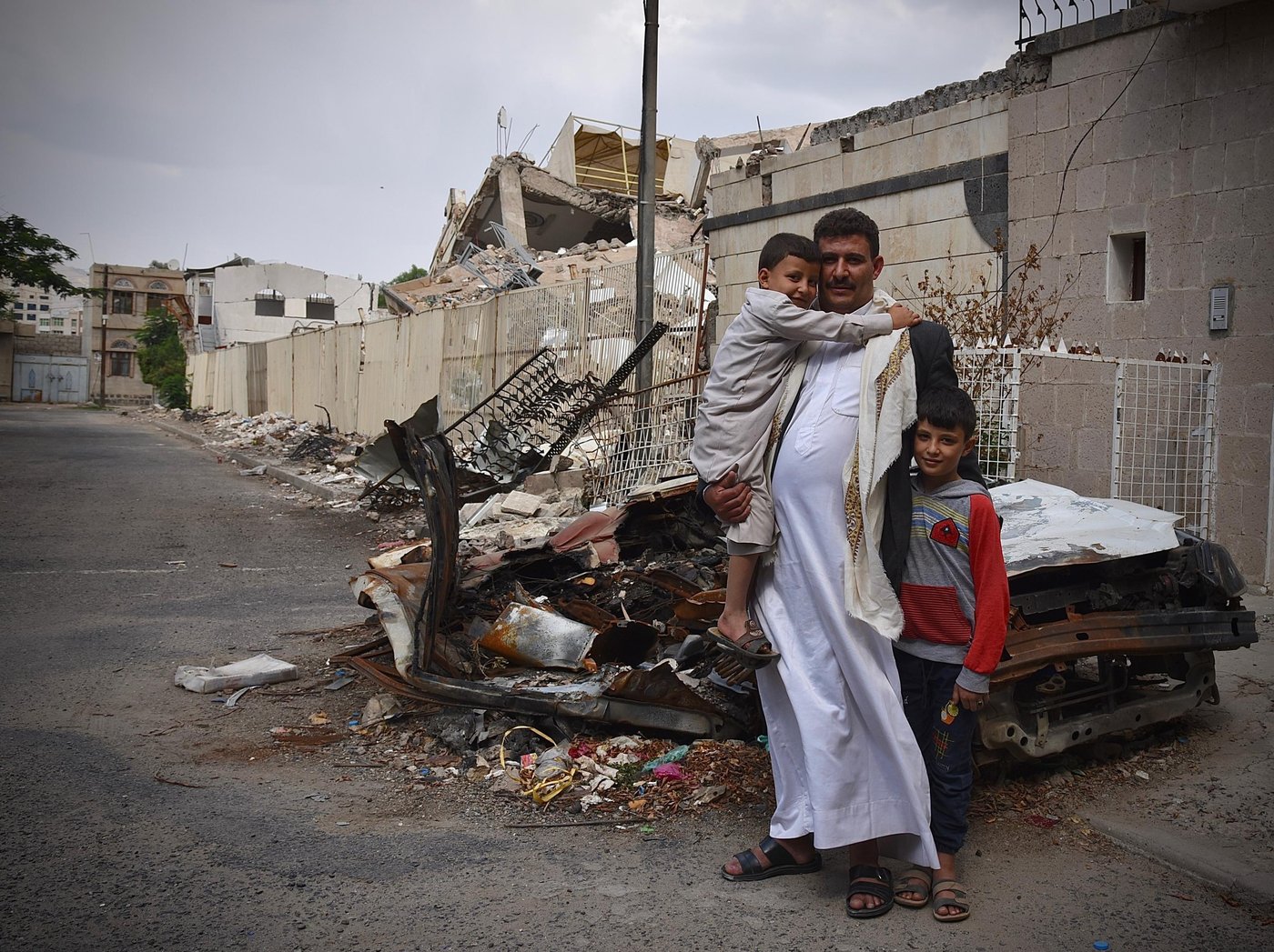 From left: Children Khalid (6), father Abdulrahman and Saif (11). 

“God forbid, I could have died that evening.”

Abdulrahman is the father of three young children and works as a compound guard for a local organisation in the Haddah neighbourhood in Sana’a. The family live right next to the compound in a guard’s house. 

On the evening of 5 June at around 9pm during Ramadan, the family were inside their house resting. Abdulrahman sent his youngest son across the road to bring water. Usually, Abdulrahman himself would be outside wandering around the area, but this evening he decided to stay in. Only minutes after his son arrived back home with the water the family heard a loud explosion and felt their house violently shake. It was the sound of a bomb that had just been dropped within metres of their home by a Saudi-led coalition aircraft.  

“The first bomb they dropped did not explode. Two or three minutes later, the second bomb was dropped and we got very afraid and tried to secure ourselves inside the house,” Abdulrahman said.

Abdulrahman moved towards the window to try to see if he could assess the damage. 

“That’s when the third bomb was dropped. I was thrown back against the wall as the window of our house exploded. We ran down to the basement. My children were screaming for their lives at this point; it felt like complete horror.”

Abdulrahman got fragments of the window glass in his leg. As the family reached the basement, a fourth bomb exploded and caused the two-story concrete structure next door to implode. The family that live their had travelled away in advance of the Eid holiday.

“We never expected something like this to happen so close to our home. My youngest son still runs to a corner and hides whenever he hears planes hovering above us. We had to take them away from this area and our house for a while to allow them time to process.” 

The attack injured seven civilians including four children. It also damaged several houses, including a neighbouring house rented by NRC for our expatriate staff, with staff inside at the time. 

Photo: Becky Bakr Abdulla/NRC