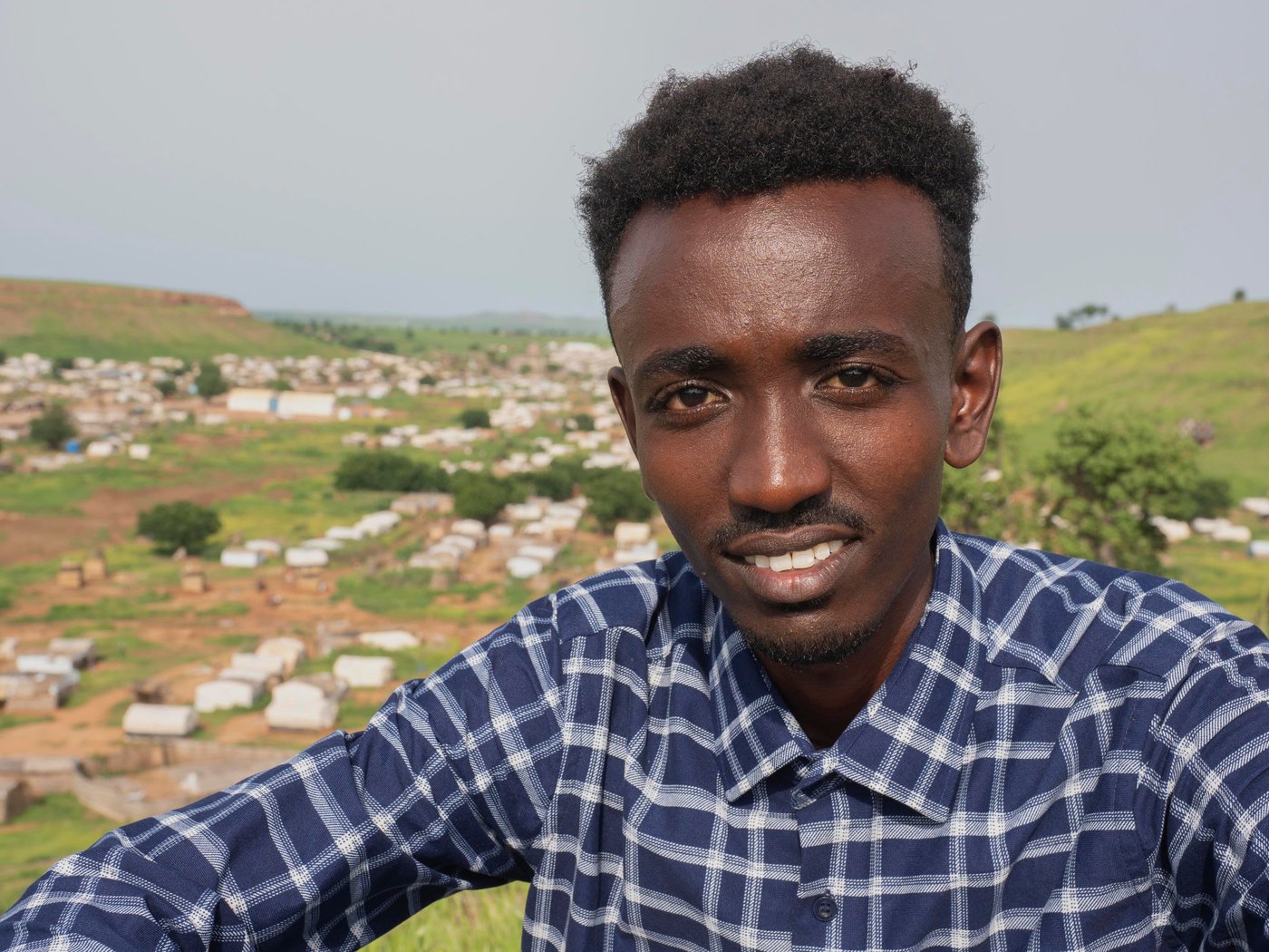 In November 2020 Aklilu packed his bags for a trip from his university in Addis Ababa, the capital of Ethiopia, to meet his family in Humera, a small town nestled in the most northwestern part of the country. Like other soon-to-be college graduates, Aklilu was already job hunting and planning to celebrate. “I’ll see you in five weeks for our graduation ceremony,” Aklilu told his friends.
A few days after Aklilu returned to his family home in Humera, mortar-fire ripped through the small town. Conflict started between the federal government of Ethiopia and the Tigrayan Defence Force. Aklilu hurried across the border into Sudan for safety. Today, over 60,000 Ethiopians have poured into Sudan for safety like Aklilu.
Aklilu fled into Sudan with nothing and left his education in Ethiopia behind. Once proficient in the backroom politics of Chelsea football club and a top structural engineering student, Aklilu kicks dirt and waits for updates about the war in Ethiopia. He wonders if the past five years of college education have been for nothing.
“We never expected this could happen. I had heard there were issues, but to me they were just politics. I never knew things could become this bad,” Aklilu says.
When Aklilu arrived at the Um Rakuba refugee camp he lived with his mother, brother, grandmother, aunt, uncle and cousins under a blue tarp that hung over bundled-together wood. A latrine was nearby and the smell overtook the morning coffee his grandmother made. A few weeks later, his family relocated to another space and were given a white tent with a gracious opening in the front and back. But in the rainy season the tent became a parachute. Aklilu and other refugees became bleary eyed by holding the tent down each night to stave off the winds.
“When I was in Ethiopia, I loved the rainy season. You can’t do anything but sit and watch the rain come down. That was my favourite moment,” says Aklilu.
Around 1,655 other university students feel abandoned in the refugee camps like Aklilu. In Umm Rakuba there are 76 university students who have formed a group, called the Tigrayan Refugees University Students in Sudan Association, or TRUSS. The association’s document lay out why their future is in doubt.   
“Going back is like choosing death,” one letter the association wrote to a visitor says. “Universities in Tigray are highly damaged and destroyed…universities outside of Tigray are giving services at this time but most Tigrayan University students are afraid to go there because of their identity." Youth like Aklilu cannot back home to continue their education in the universities of Ethiopia in fear of the violence and discrimination they might encounter for being Tigrayans.
“A result of the conflict in Ethiopia is that some of the brightest minds in the country are confined to refugee camps in Sudan,” said Will Carter, Sudan Country Director at the Norwegian Refugee Council. “If these students are given a chance somewhere, they’d be a spark for whomever accepts them.”


But TRUSS students want more than acceptance into a University — they want a university to recognize their past work.
Many hurdles stand in the way of Aklilu getting his degree. When the violence started, many like Aklilu fled and left behind most of their valuables, including their civil documents, identity cards, and education records. As result, they are now unable to provide proof for who they are or how far along they got in university. Also, in a camp where the scarce amount of money they have is barely enough for food, the students cannot afford paying for registration, books, transportation, and accommodation.  The only solution would be a full-board scholarship.
Recently, Aklilu has been exploring going to a university in Ghana under a scholarship. However, this scholarship likely means that students lose the progress they have made in university and start from scratch. 
Aklilu, like the other senior students in the camp, is frustrated that he probably has to spend another five years studying for a Civil Engineering Degree he was only five weeks away from receiving.
“We are waiting for the opportunity for a university that will accept to acknowledge the credit we have from the university back home. If we accept to start over, we will be 30 years old by the time we graduate. We might not find a job for a long time over. We will be wasting a lot of time in our life,” says Aklilu.On a Friday morning, members of the association gather in a communal tent for their weekly meeting. They have organized themselves into committees and are planning their week ahead. One group will fundraise among other refugees to help an isolated elderly woman in the camp; another one will meet other students and youth in the camp to connect them with NGOs.
While they wait for education, the students in TRUSS and other youth act like community mobilizers. Truss has been helping organizations like NRC to re-build shelters, organize cash distributions, facilitate children registration in school, as well as raising community issues. They receive stipends from organizations, which help them support their families. 
“I liked watching movies and series back home, but I like it even more now because there’s nothing much else to do,” says Bisrat, one of Aklilu’s close friends, who now works for NRC.
The students feel trapped in part because they are. The 2014 Asylum Act gives refugees the right to move and seek an education, but in reality, they are contained to the camp. The encampment policy enforced for refugees prevents all the residents to leave the site, cutting them access to jobs and markets and curtailing their freedom of movement.
“Tigrayan refugees cannot leave the camp unless they acquire a permit from authorities for worthy reasons, linked to education, health, or jobs. Unfortunately, these permits are very hard to get – it becomes a vicious circle. They can’t get many opportunities to leave the camp, if they can’t leave the camp to look for them,” says Silvia Beccacece, former NRC Gadarif Area Manager.
Kids in the camp get access to education but are not much better off. Thanks to help from the Norwegian Ministry of Foreign Affair, NRC was one of the first organizations to respond to learning needs in Umm Rakuba. Since then, NRC has been able to expand the quality and durability of the schools with the help of Education Cannot Wait. Around 2,050 children, aged between 6 and 14, go to the four schools NRC has built in different areas of the camp. Resources remain limited. The only textbooks available were ferried across from Ethiopia, and the children attend their classes by sitting on the floors of sand.
Still, students are grateful for what they receive. Nati Teame, 10, is one of NRC’s schoolchildren in the Um Rakuba camp. 
“I wake up in the morning and pass the time until it’s time for school. I’ve never been late,” Nati said. “My parents never got the chance to be educated, and I don’t want the same thing to happen to me.”

Photo: Ingrid/Prestetun