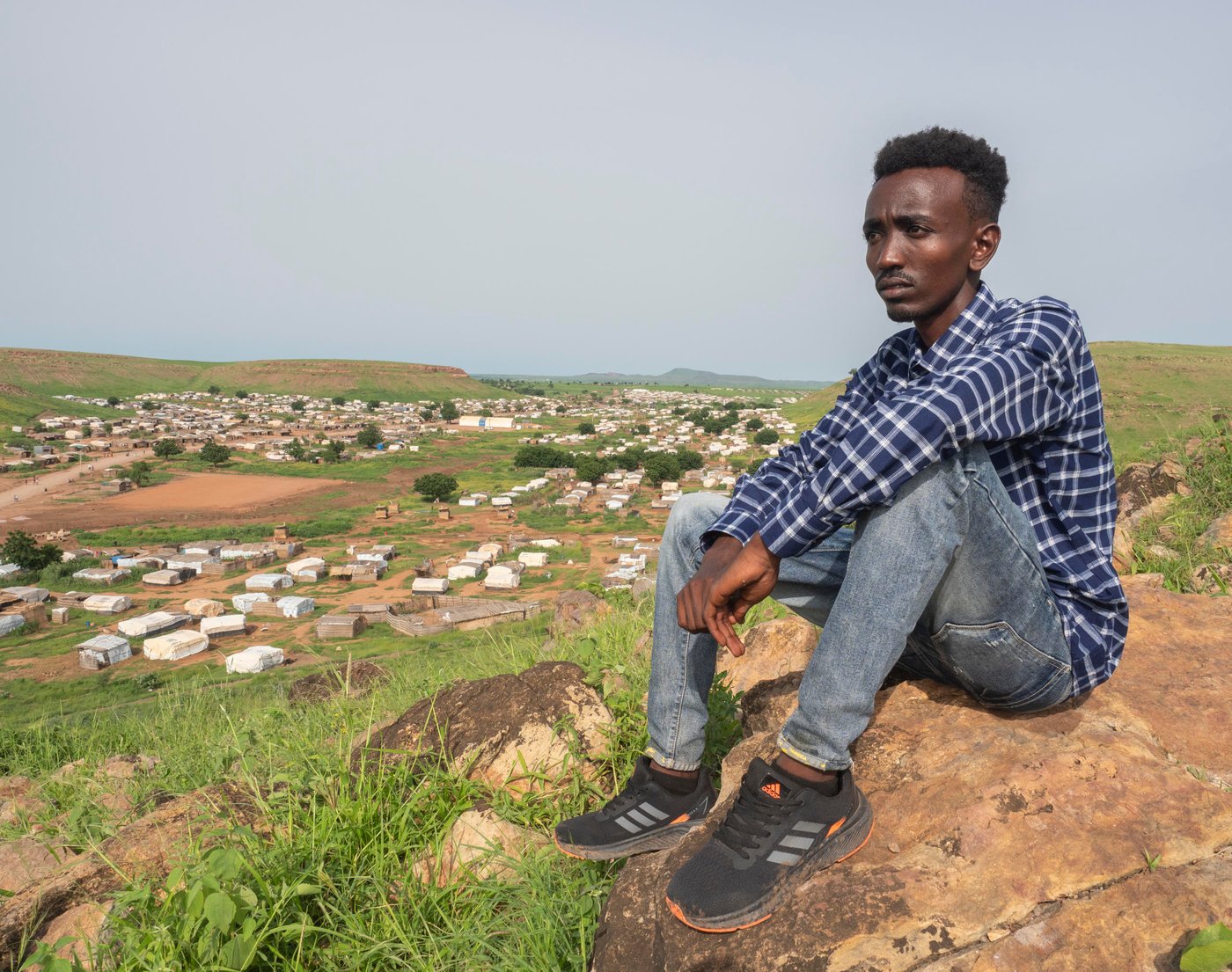 In November 2020 Aklilu packed his bags for a trip from his university in Addis Ababa, the capital of Ethiopia, to meet his family in Humera, a small town nestled in the most northwestern part of the country. Like other soon-to-be college graduates, Aklilu was already job hunting and planning to celebrate. “I’ll see you in five weeks for our graduation ceremony,” Aklilu told his friends.
A few days after Aklilu returned to his family home in Humera, mortar-fire ripped through the small town. Conflict started between the federal government of Ethiopia and the Tigrayan Defence Force. Aklilu hurried across the border into Sudan for safety. Today, over 60,000 Ethiopians have poured into Sudan for safety like Aklilu.
Aklilu fled into Sudan with nothing and left his education in Ethiopia behind. Once proficient in the backroom politics of Chelsea football club and a top structural engineering student, Aklilu kicks dirt and waits for updates about the war in Ethiopia. He wonders if the past five years of college education have been for nothing.
“We never expected this could happen. I had heard there were issues, but to me they were just politics. I never knew things could become this bad,” Aklilu says.
When Aklilu arrived at the Um Rakuba refugee camp he lived with his mother, brother, grandmother, aunt, uncle and cousins under a blue tarp that hung over bundled-together wood. A latrine was nearby and the smell overtook the morning coffee his grandmother made. A few weeks later, his family relocated to another space and were given a white tent with a gracious opening in the front and back. But in the rainy season the tent became a parachute. Aklilu and other refugees became bleary eyed by holding the tent down each night to stave off the winds.
“When I was in Ethiopia, I loved the rainy season. You can’t do anything but sit and watch the rain come down. That was my favourite moment,” says Aklilu.
Around 1,655 other university students feel abandoned in the refugee camps like Aklilu. In Umm Rakuba there are 76 university students who have formed a group, called the Tigrayan Refugees University Students in Sudan Association, or TRUSS. The association’s document lay out why their future is in doubt.
“Going back is like choosing death,” one letter the association wrote to a visitor says. “Universities in Tigray are highly damaged and destroyed…universities outside of Tigray are giving services at this time but most Tigrayan University students are afraid to go there because of their identity." Youth like Aklilu cannot back home to continue their education in the universities of Ethiopia in fear of the violence and discrimination they might encounter for being Tigrayans.
“A result of the conflict in Ethiopia is that some of the brightest minds in the country are confined to refugee camps in Sudan,” said Will Carter, Sudan Country Director at the Norwegian Refugee Council. “If these students are given a chance somewhere, they’d be a spark for whomever accepts them.”
But TRUSS students want more than acceptance into a University — they want a university to recognize their past work.
Many hurdles stand in the way of Aklilu getting his degree. When the violence started, many like Aklilu fled and left behind most of their valuables, including their civil documents, identity cards, and education records. As result, they are now unable to provide proof for who they are or how far along they got in university. Also, in a camp where the scarce amount of money they have is barely enough for food, the students cannot afford paying for registration, books, transportation, and accommodation. The only solution would be a full-board scholarship.
Recently, Aklilu has been exploring going to a university in Ghana under a scholarship. However, this scholarship likely means that students lose the progress they have made in university and start from scratch.
Aklilu, like the other senior students in the camp, is frustrated that he probably has to spend another five years studying for a Civil Engineering Degree he was only five weeks away from receiving.
“We are waiting for the opportunity for a university that will accept to acknowledge the credit we have from the university back home. If we accept to start over, we will be 30 years old by the time we graduate. We might not find a job for a long time over. We will be wasting a lot of time in our life,” says Aklilu.On a Friday morning, members of the association gather in a communal tent for their weekly meeting. They have organized themselves into committees and are planning their week ahead. One group will fundraise among other refugees to help an isolated elderly woman in the camp; another one will meet other students and youth in the camp to connect them with NGOs.
While they wait for education, the students in TRUSS and other youth act like community mobilizers. Truss has been helping organizations like NRC to re-build shelters, organize cash distributions, facilitate children registration in school, as well as raising community issues. They receive stipends from organizations, which help them support their families.
“I liked watching movies and series back home, but I like it even more now because there’s nothing much else to do,” says Bisrat, one of Aklilu’s close friends, who now works for NRC.
The students feel trapped in part because they are. The 2014 Asylum Act gives refugees the right to move and seek an education, but in reality, they are contained to the camp. The encampment policy enforced for refugees prevents all the residents to leave the site, cutting them access to jobs and markets and curtailing their freedom of movement.
“Tigrayan refugees cannot leave the camp unless they acquire a permit from authorities for worthy reasons, linked to education, health, or jobs. Unfortunately, these permits are very hard to get – it becomes a vicious circle. They can’t get many opportunities to leave the camp, if they can’t leave the camp to look for them,” says Silvia Beccacece, former NRC Gadarif Area Manager.
Kids in the camp get access to education but are not much better off. Thanks to help from the Norwegian Ministry of Foreign Affair, NRC was one of the first organizations to respond to learning needs in Umm Rakuba. Since then, NRC has been able to expand the quality and durability of the schools with the help of Education Cannot Wait. Around 2,050 children, aged between 6 and 14, go to the four schools NRC has built in different areas of the camp. Resources remain limited. The only textbooks available were ferried across from Ethiopia, and the children attend their classes by sitting on the floors of sand.
Still, students are grateful for what they receive. Nati Teame, 10, is one of NRC’s schoolchildren in the Um Rakuba camp.
“I wake up in the morning and pass the time until it’s time for school. I’ve never been late,” Nati said. “My parents never got the chance to be educated, and I don’t want the same thing to happen to me.”
Photo: Ingrid/Prestetun