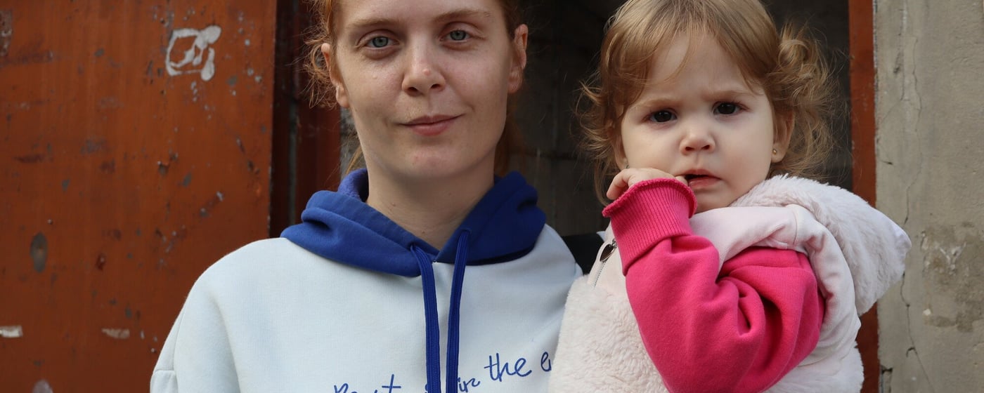 Anastasiia tillsammans med sin dotter utanför familjens hem i Derhachi i Charkivregionen. Huset skadades av beskjutning, och det är svårt att hålla det varmt under vintern. Foto: Inha Musiiuk/NRC