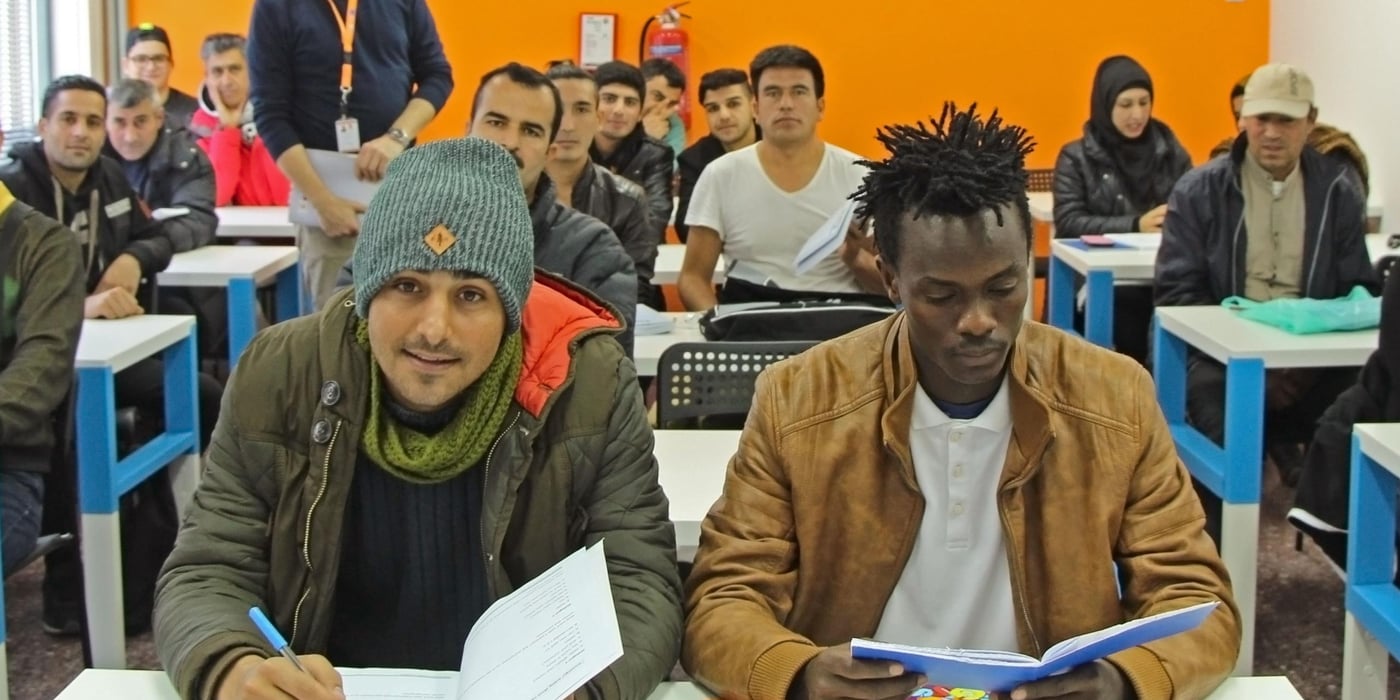 Sekou Kumara (right), 18, sits at the front of his English class in Thessaloniki as teacher Vassilis Papadopoulos looks on. Photo: Maria Gounaridou/NRC