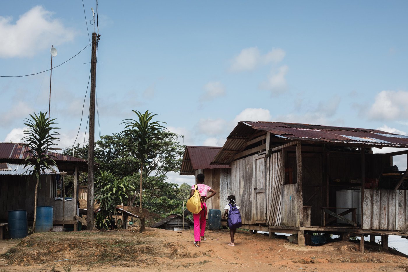 Två flickor går till skolan längs en jordväg mellan trähus i en by i Chocó i västra Colombia. Området hör till de regioner där Norwegian Refugee Council har dokumenterat många attacker mot utbildning.