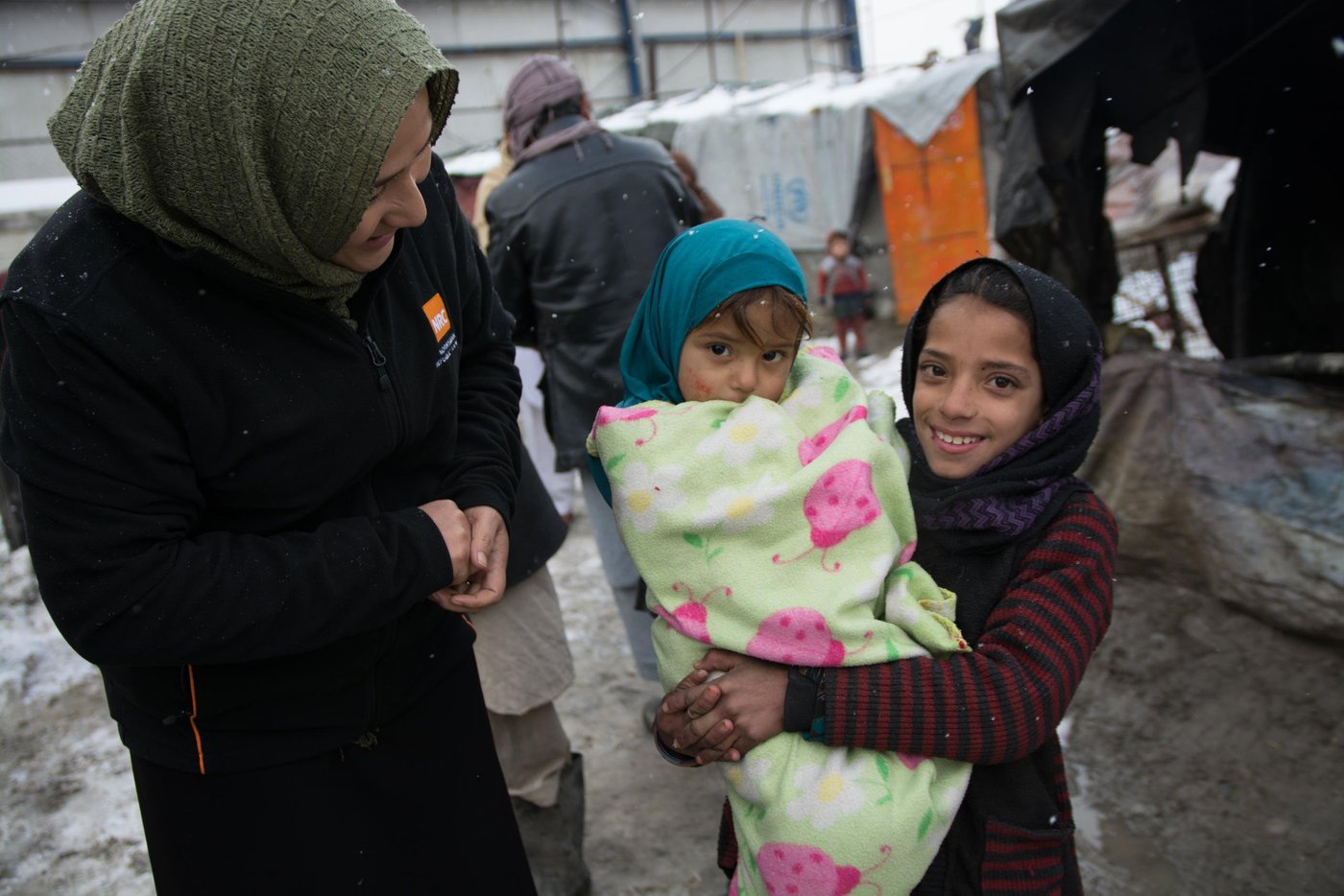 NRC's shelter technical assistant Masooma Qambari, talking to Nazia, 11, taking care of her little sister wrapped in a thick blanket in one of the informal settlements in Kabul. The children are experiencing their third winter in this settlement. photo: NRC/Enayatullah Azad