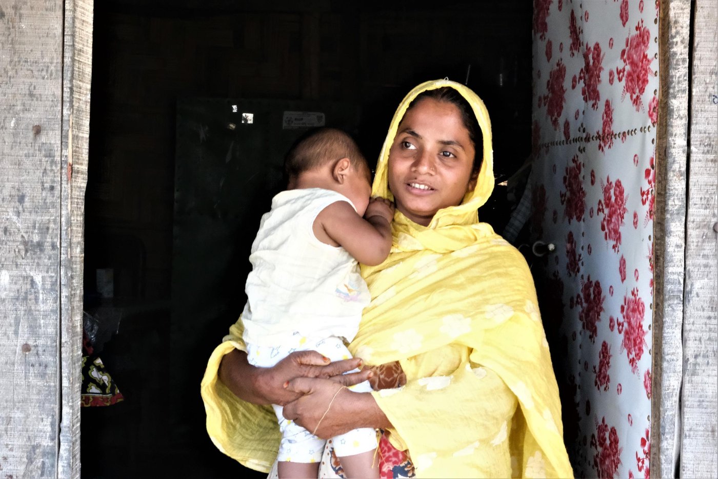 Rohima with one of her children in front of their small, thatched home. Photo: Ayesha Nawshin/NRC