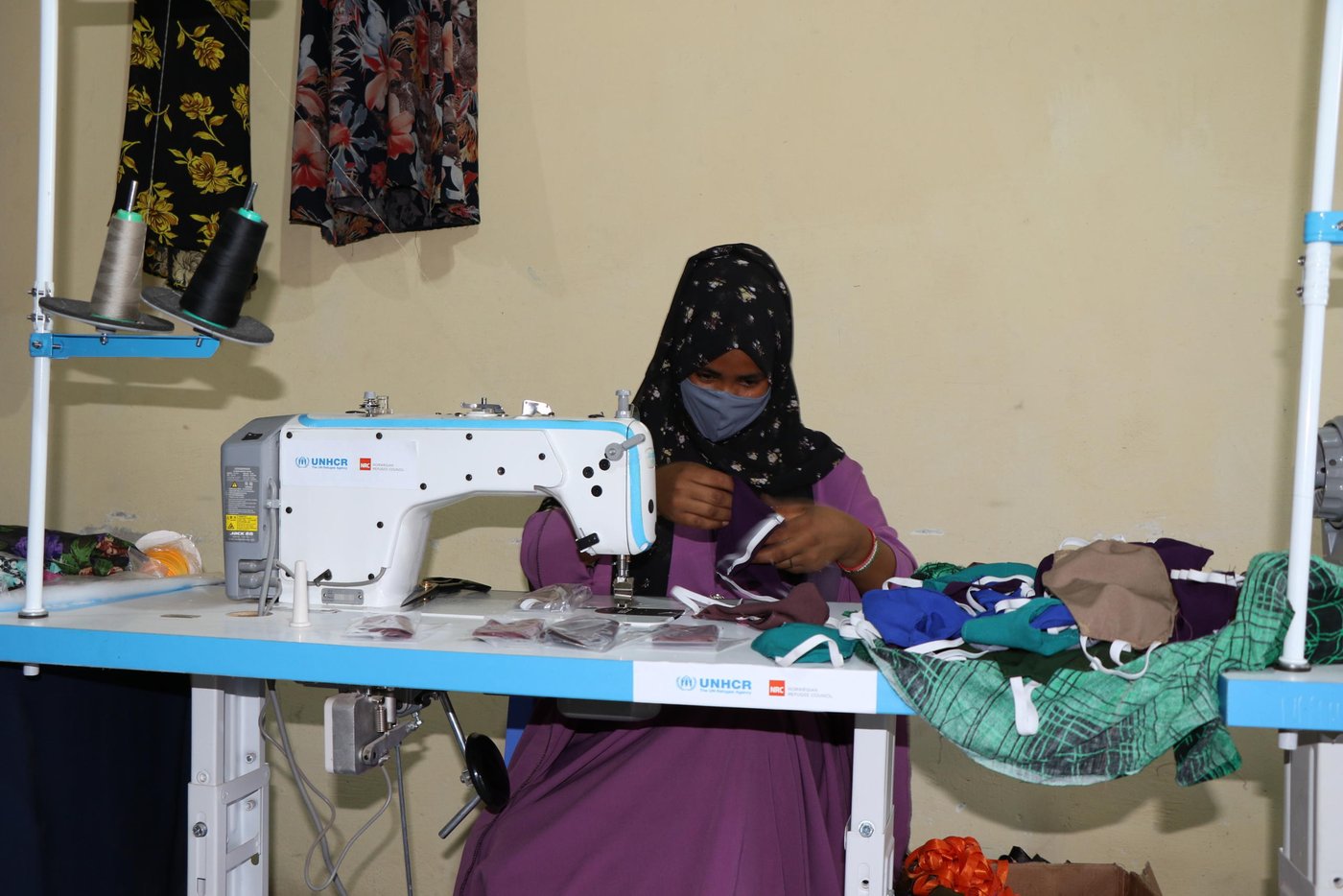Hafsa is 22 years old young girl. She lives in Hargeisa with her family. Hafsa and her family have previously been displaced from Ethiopia and lived in Somaliland for so many years. She was one of the youths selected from the IDPs, refugees & asylum seekers project in Somaliland for a tailoring course, which is one of the vocational skill courses (Tailoring, Carpentry, Plumping, Electricity, Soap Production, Plastic Recycling, Painting & Decoration) under NRC’s livelihood project funded by UNHCR.
The project targets the vulnerable youths who have had limited access to training and employment opportunities, providing them the opportunity to attain well-planned vocational skills that enhance their ability to access and engage in livelihood opportunities. Hafsa is among young men and women who have already graduated from NRC’s vocational skills course. She is currently utilizing the previously attained skills in both employment and private engagement, enabling her to earn a decent income.
Hafsa says, “I am a tailor, and tailoring was always my favorite. I have got information that NRC and UNHCR are registering students for vocational skill courses. I went to the registration center. Fortunately, I was registered for the tailoring course. I was learning for around eight months. I really thank NRC and UNHCR for the tailoring course. After I had completed the course, I became one of five women who received investment money and sewing machines from NRC. We’ve established this tailoring shop. We sell and make clothes. After a short while, the COVID-19 pandemic has broken out in the country. Then we shifted our products into face mask production, which was very important and was actually a very good source of income for us. Students are now our main customers. We still produce other clothes for men and women, but face masks are our main products”.
Photo: Abdulkadir/NRC.