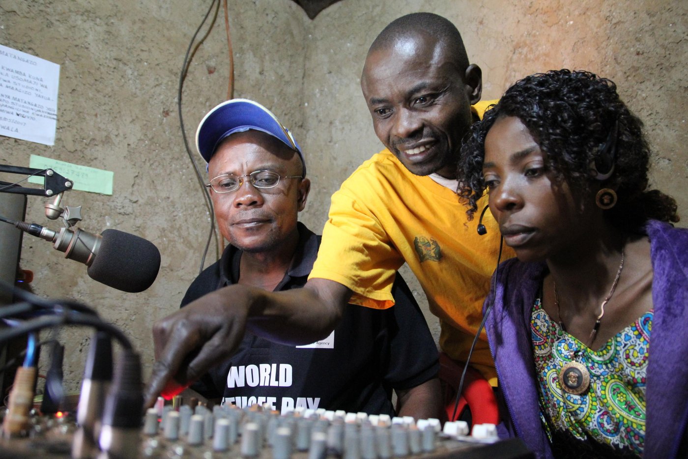 Radio Umoja was established by Jonathan (in yellow t-shirt) in March 1997. When he first entered Nyarugusu refugee camp, he observed that there was a lot of misinformation or lack of information reaching refugees on issues affecting them. He immediately swung into actions. Using available resources, he acquired a loud speaker and a small transmitter and during the evening he would announce information that he had acquired through UNHCR and other agencies through the loudspeaker. Many people used to come to gather around the loudspeaker to listen to latest information.

Gaining acceptance and support, he started putting together radio station equipment through support from humanitarian agencies. He also obtained a 6-month license from the Tanzanian government to broadcast information. During the six-month pilot phase, he received supervision and content scrutiny from Tanzania’s Ministry of Home Affairs. 

He used to get permits to stay out of the camp in order to travel to Dar-es-Salaam capital to follow up on equipment such as transmitters, microphones and studio controls. He also received permits to bring on board radio announcers and field reporters.
His main goal is to use the radio station to raise awareness among the refugee population about pertinent issues and solutions. For example, how the youth can be productive and avoid engaging in criminal activities. He also speaks out against sexual violence targeting women and girls. The radio transmitter covers a radius of 30 kilometres. “People in Nyakitonto usually call the studio to say that they can hear our voices loud and clear,” says Jonathan.

Initially his radio station was called ‘Radio Taarifa Tangazo na Salaam’ (RTTS), translated as News, Announcement and Greetings Radio.  Later he decided to specialize in religious songs and changed the name to Umoja Radio, which means Unity radio. There are 26 workers in the studio, including security staff, editors, cleaners, field reporters among others. These are all volunteers. 

Operational challenges

“Lack of funds to pay workers and services that we receive is the biggest challenge. This leads to a high turn-over since the workers also need an income to support their families,” says Jonathan. This means that the radio station cannot operate optimally since fuel shortage are bound to occur. 15 litres of petrol is needed per day to guarantee full-time broadcast, while a litre of petrol costs 2,500 Tanzanian Shillings (XXX US Dollars). Jonathan has a better idea, he thinks that solar as an alternative green power option can solve all the energy and fuel demands.
As can be expected from a remote refugee camp like Nyarugusu, there are other challenges faced by the radio station staff. “The station infrastructure needs an upgrade. We need to fix the ceiling, buy office facilities such as tables, chairs, shelves, monitors and central processing units. We are also using an improvised antennae to transmit radio frequencies,” says Jonathan. Most importantly, they need money to pay for transport for field reporters, or to purchase a scooter for ease of transportation.

Umoja Radio broadcasts from 6am up to midnight on Sundays to Thursday and 24 hours on Fridays and Saturdays. However, due to shortage of fuel, radio hours can sometimes be shortened. To subsidize running costs, they sometimes sell greeting cards and on-air advertisements. “Listeners are not happy when we shorten the radio hours,” says Jonathan.
The most popular programmes are “Vijana na Maendeleo” (youth and development), “Sauti ya walemavu” (voices of people with disabilities), “Wakati wa utamaduni” (Time for traditions) and “Afya yetu” (Our health). Except for one, all other programmes are broadcast in Swahili language which is well understood by both refugees and host communities. They also publish a monthly magazine called “Mwangaza” which means “Rays of light”.

Community engagement

According to Jonathan, it is very important to work closely with the refugee community and be seen to be part of camp activities. We cannot afford to operate in isolation, any perception of being an ivory tower automatically leads to loss of trust. For example, a children’s parliament visits the radio station once every term to discuss and debate issues. Listeners can also call in and express their views.

The station is running broadcast courses for students who are interested in journalism. The third cycle of courses has been started with a total of 21 students. Twenty-one learners completed the first cycle, followed by 17 students on the second cycle. They hope to secure their own building structures to offer the courses. Subjects taught include History of radio and broadcasting, language of radio, communication processes, broadcasting chain, interview techniques, radio production, advocacy and media ethics.

Radio staff regularly visit local hospitals to speak with patients and discuss health issues. These inform health programmes such as ‘Ugua pole’ translated as ‘quick recovery’. However, at times the hospital staff and management become hostile towards field reporters and put a ban on speaking to the media. They also visit farmers to better understand their livelihood activities and farming methods.

“Generally the host communities perceive refugees as troubled people who have fled their country and cannot depend on themselves for daily survival. We are also perceived as people whose movements are restricted, which is a challenge when we try to access services. When I used to travel to Dar-es-Salaam using my movement authorization people used to be suspicious when I informed them that I was a refugee. One man suspected that I was plotting a coup to overthrow the government,” he says. In addition, host communities perceive refugees as being criminals or lazy. He hopes that through his programmes, he can help to reverse the negative attitudes.

Online radio

Interestingly, Umoja Radio can also be heard through the internet and through mobile App ‘Umojaradio’ which can be downloaded via Googla Play. To listen to the radio via the web, go to: www.umojaradio.nl. On Facebook, the address is ‘Umoja Radio Nyarugusu’. Through the internet, they are able to reach millions of active and potential listeners. Listeners regularly send greetings from as far as the United States of America, Australia, The Netherlands and South Africa. One listener from Norway also showed up at one time. The main challenge is that they rely on a modem with a speed of just 7.2 Megabytes per second. 
Background and early days

Jonathan has spent 20 years in Nyarugusu camp. He first arrived in 1996 fleeing tribal conflict locally labelled ‘Songa Mbele’, or ‘move on’. He was born in Fizi Zone in the Democratic Republic of Congo. He is 47 years old. He started learning about radio in the DRC. He used to write articles for ‘Jua’ newspaper (Jua means Knowledge in Swahili language. He was a reporter for Radio Channel Africa from 2004 to 2005. 

Quotes from Jonathan:

"I am working here at Radio Umoja situated in the Nyarugusu refugee camp, I am happy because our radio station informs and teaches the refugees all the time. We begin our broadcast at 8am in the morning until midnight."

"It is important that refugees listen to the information through our radio. It is important because they listen to information across the world from Nyarugusu."

"Radio Umoja is independent and belongs to the refugees. This includes the refugees from Congo DR and Burundi as well."

Photo: NRC Ingrid Prestetun