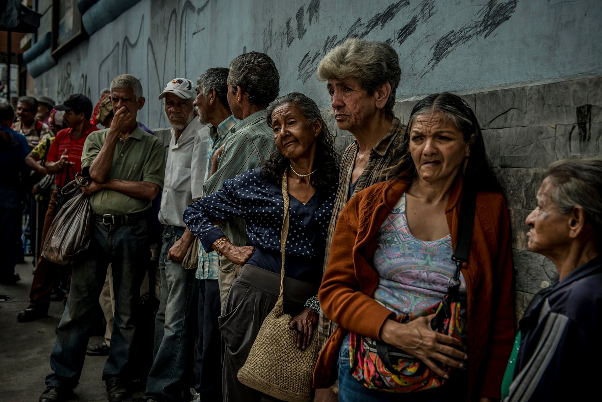 Ama Heredia, in blue blouse, and Zoraida Morales, third from right, line up for free food at a soup kitchen in Los Teques, Venezuela, Sept. 22, 2017. As a dire economy drives migration, Venezuelans in their retirement years are joining the exodus, a journey fraught with worries over health care, employment and leaving a country they once loved. (Meridith Kohut/The New York Times)