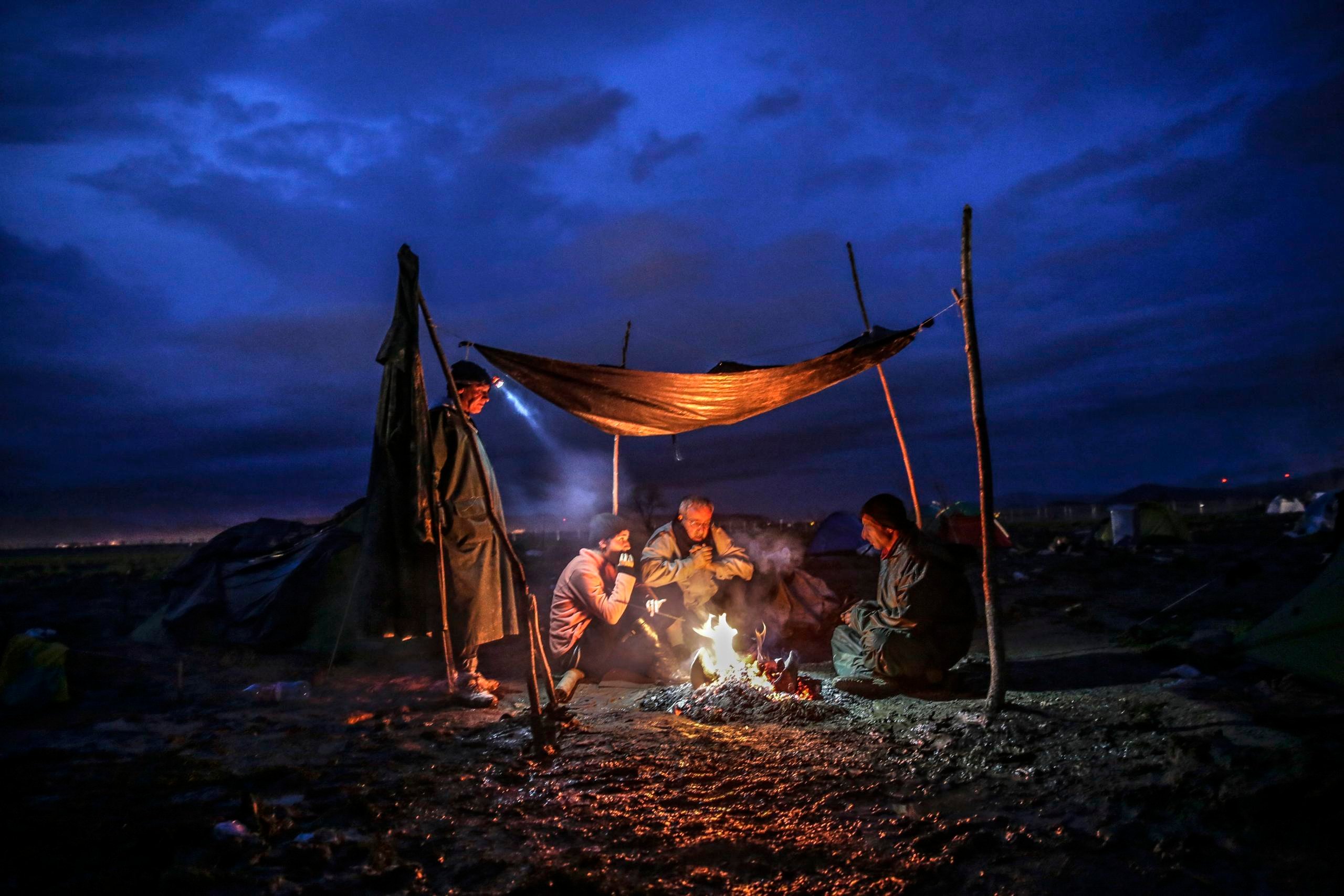 epaselect epa05205066 Refugees warm themselves by a fire at the border between Greece and the Former Yugoslav Republic of Macedonia (FYROM), near Idomeni, northern Greece, 10 March 2016. After Slovenia, Croatia, Serbia and Macedonia have sealed their borders to the migration flow, tens of thousands of people are left stranded in Greece, where most migrants enter the European Union to continue on to countries in Europe. Greece estimates that more than 25,000 migrants are presently on its territory, with more than half stuck at the makeshift camp Idomeni, on the border with Macedonia. EPA/VALDRIN XHEMAJ
