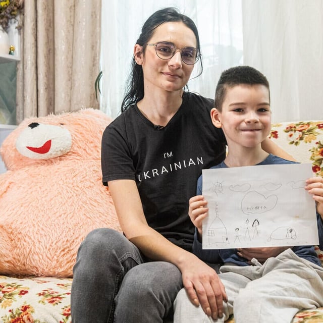 En kvinna och en pojke sitter tätt intill varandra i en soffa i ett vardagsrum. Kvinnan har armen om pojken och ser lugnt in i kameran.