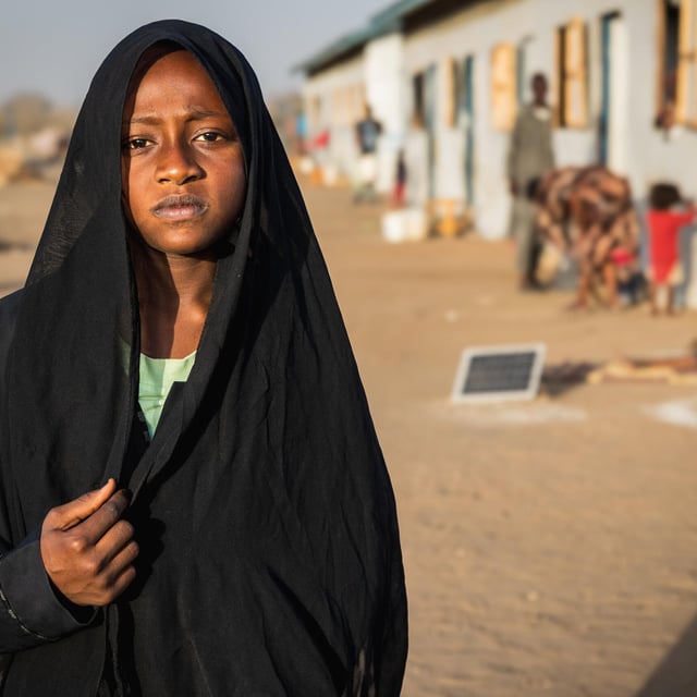 En ung kvinna står i förgrunden och ser rakt in i kameran.