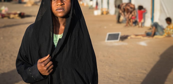 En ung kvinna står i förgrunden och ser rakt in i kameran.