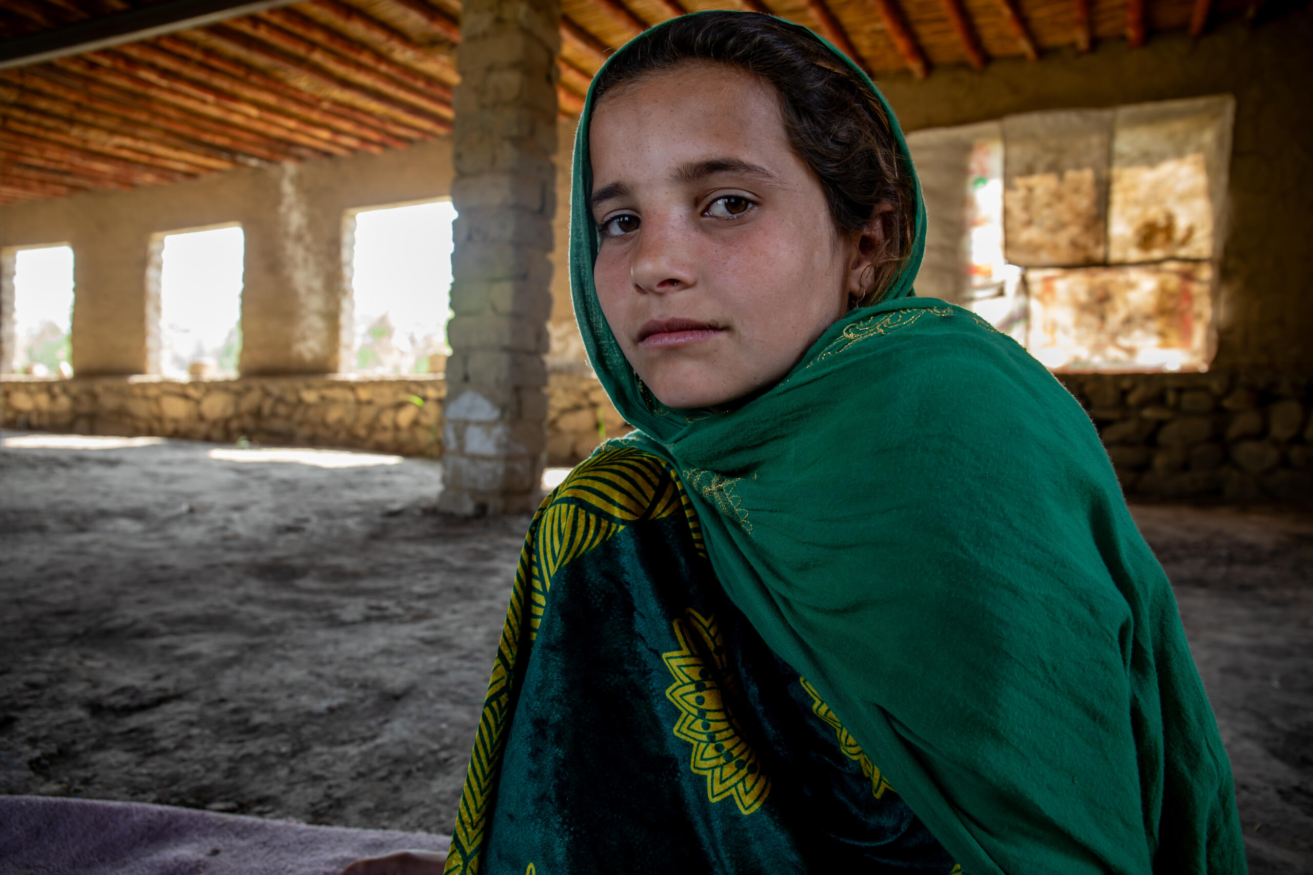En flicka sitter i en skadad skolbyggnad i Afghanistan. M&aring;nga barn p&aring;verkas av landets humanit&auml;ra kris och begr&auml;nsade tillg&aring;ng till utbildning.