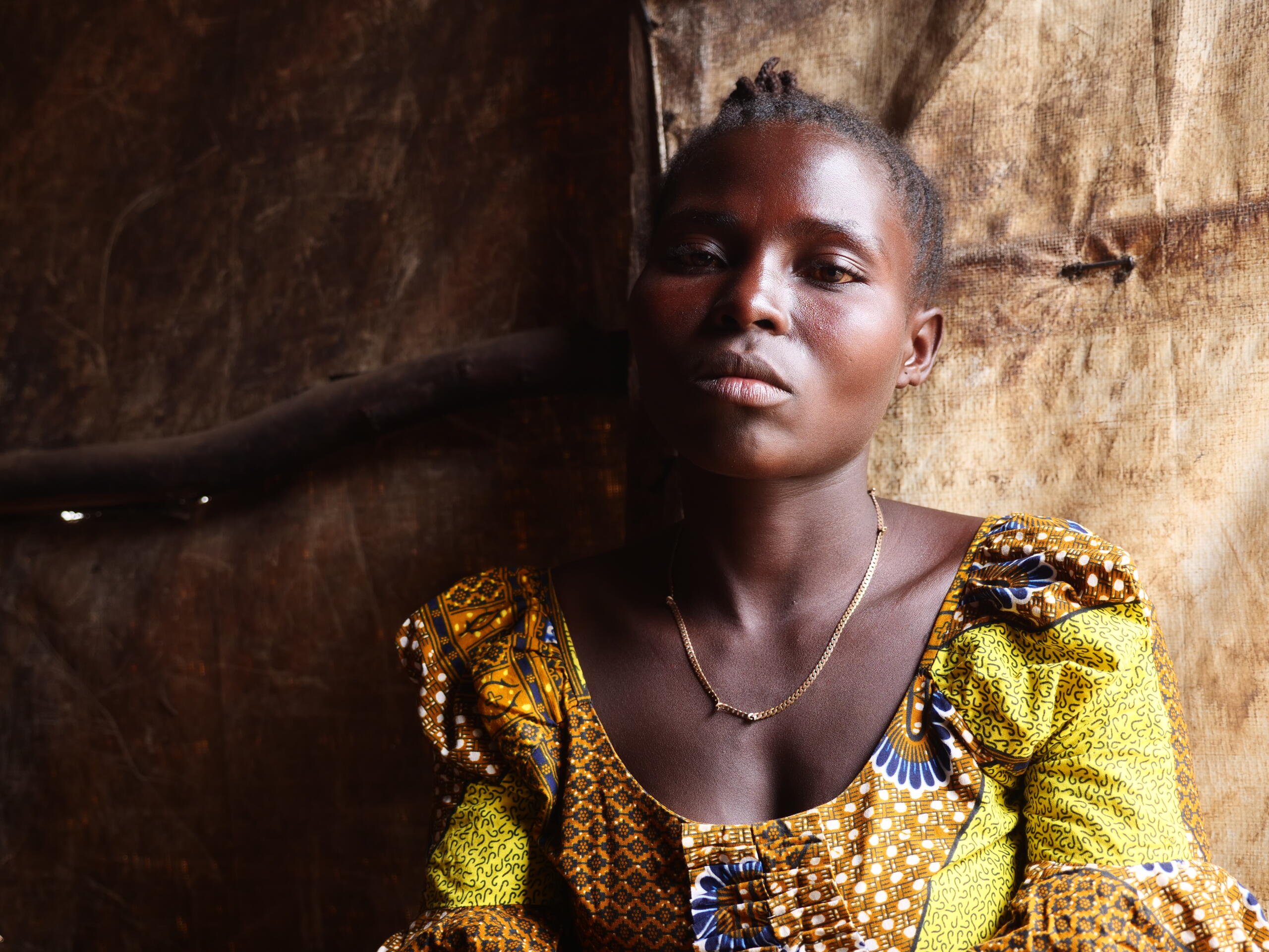 En kvinna sitter i ett enkelt skydd och ser in i kameran.