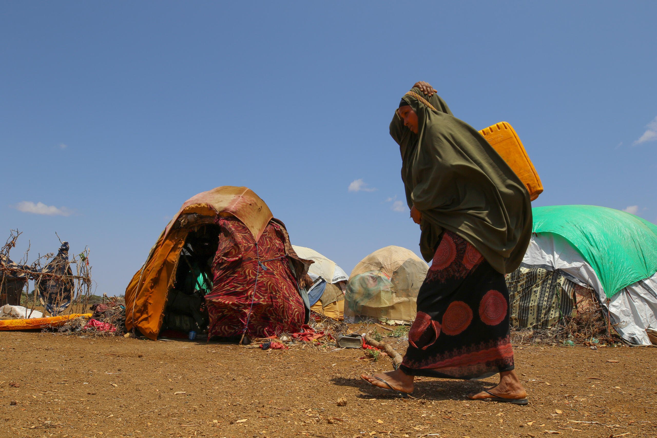 En kvinna g&aring;r genom ett tillf&auml;lligt bos&auml;ttningsomr&aring;de med vatten p&aring; ryggen.