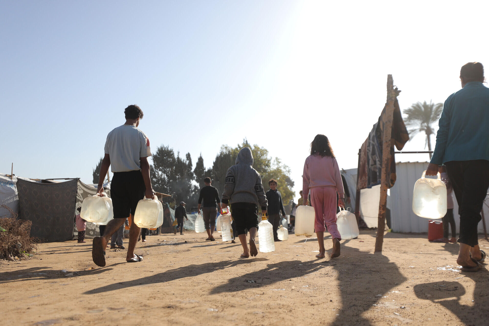 En grupp m&auml;nniskor g&aring;r l&auml;ngs en dammig v&auml;g i ett l&auml;geromr&aring;de och b&auml;r genomskinliga dunkar fyllda med vatten