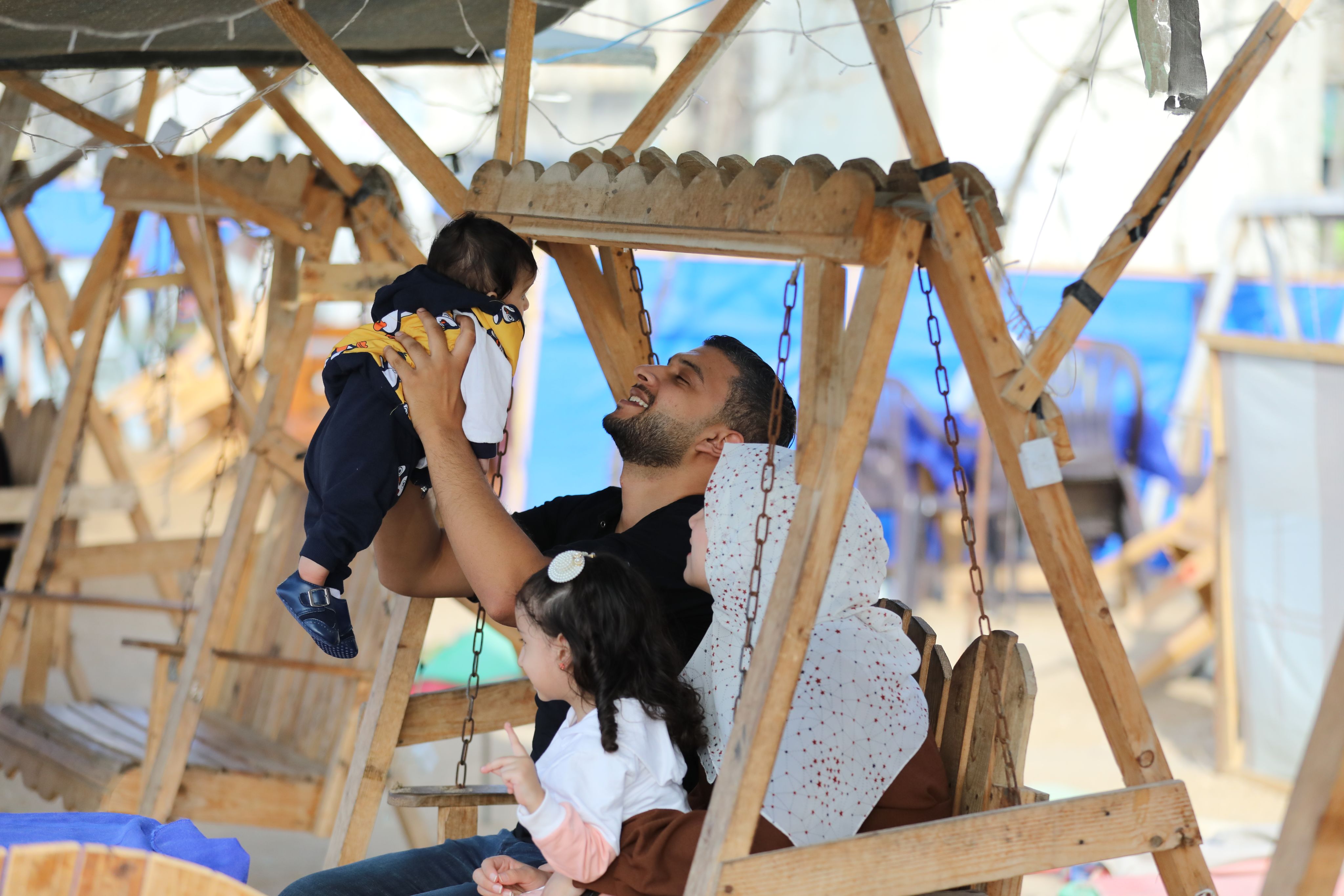 Yousef og familien sitter på et huskestativ ved en lekeplass. Yousef løfter sønnen over hodet og smiler til han.