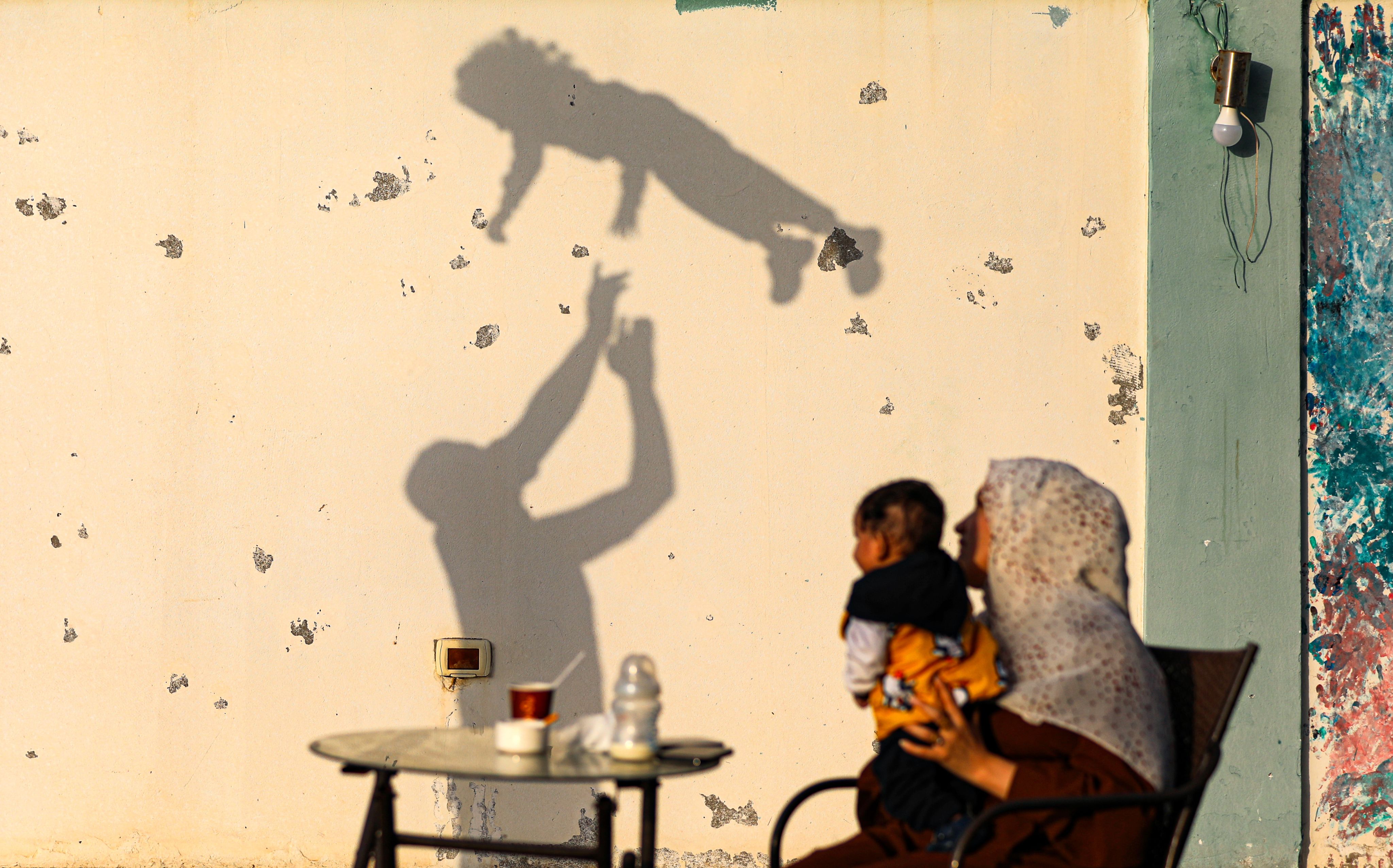 Skyggen av en mann som kaster datteren sin opp i lufta vises på en vegg. I forgrunnen sitter moren og sønnen og ser på.