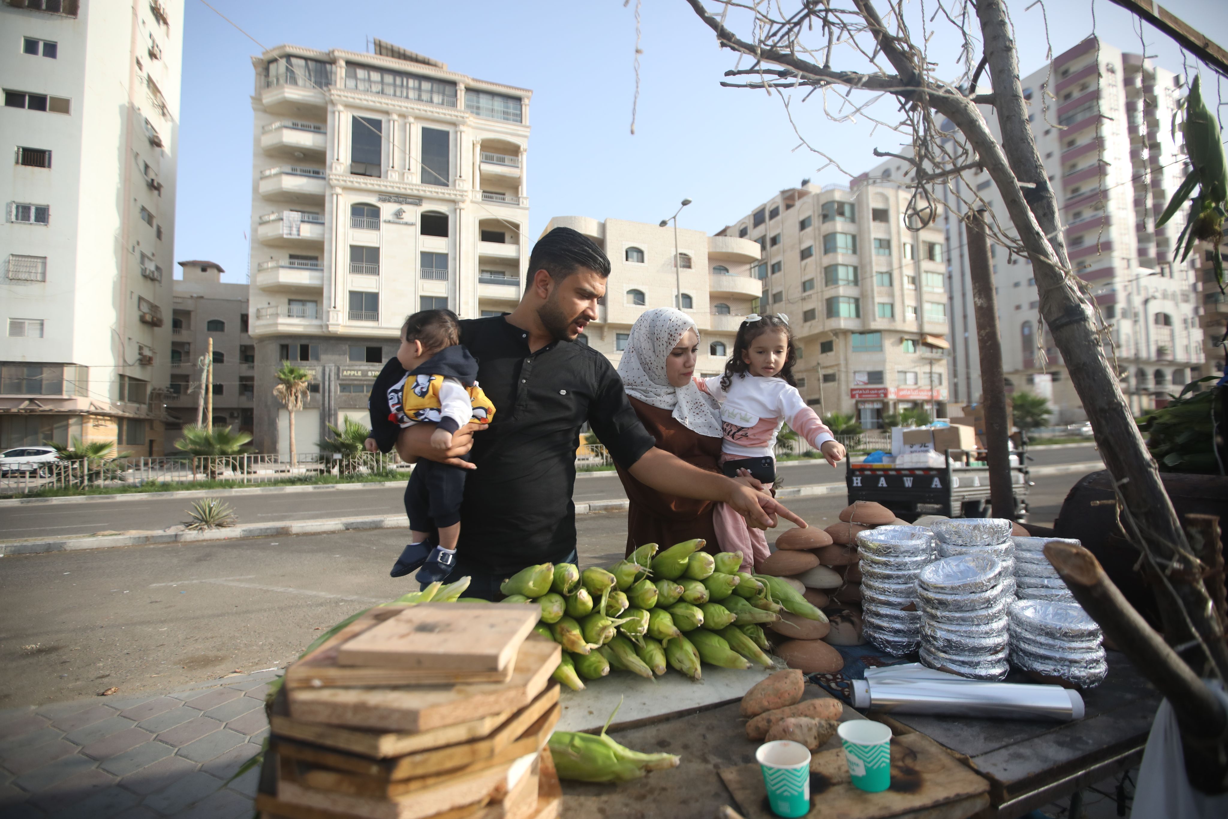 En familie på fire handler mais i en bod på gaten. Varene ligger stablet oppå hverandre, og faren peker på det de ønsker å kjøpe.