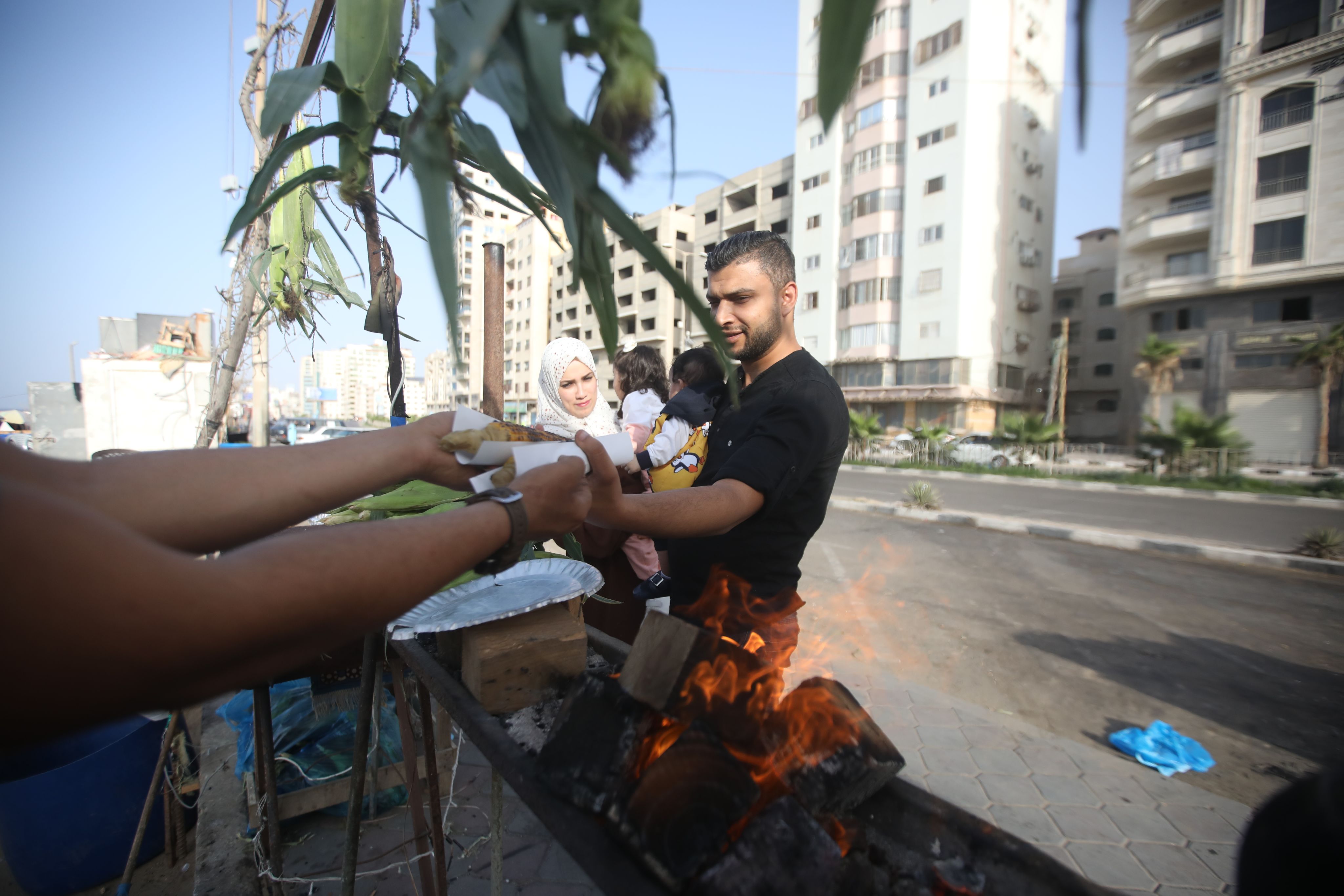 En kjøpmann leverer ut to maiskolber som er tilberedt over åpen flamme i boden sin. Faren i en familie på fire tar imot maten.