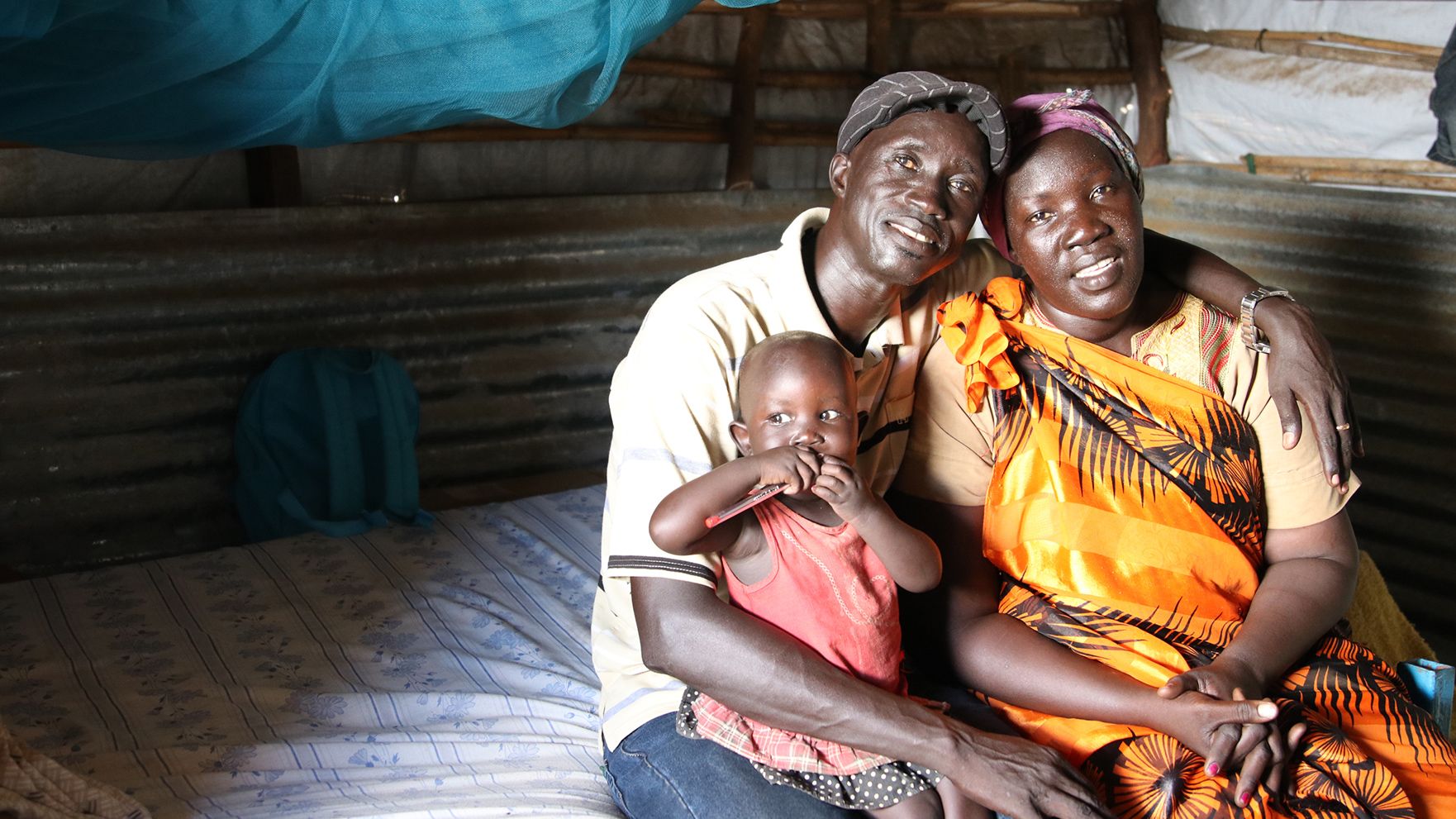 Majok holds his arm around his wife, Teresa. They are both smiling. Their youngest daughter is sitting on Majok's lap.