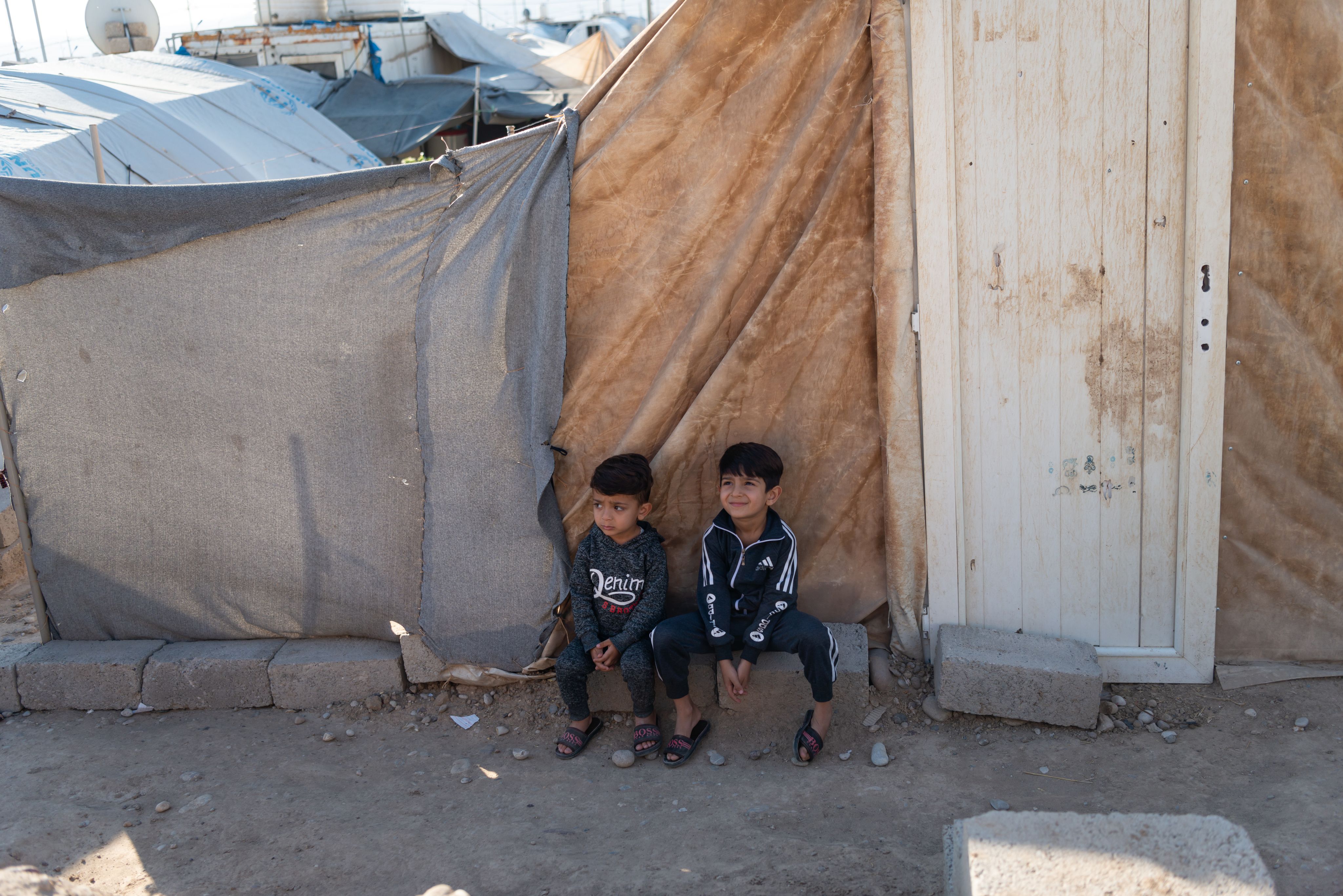Two young boys sit in refugee camp.