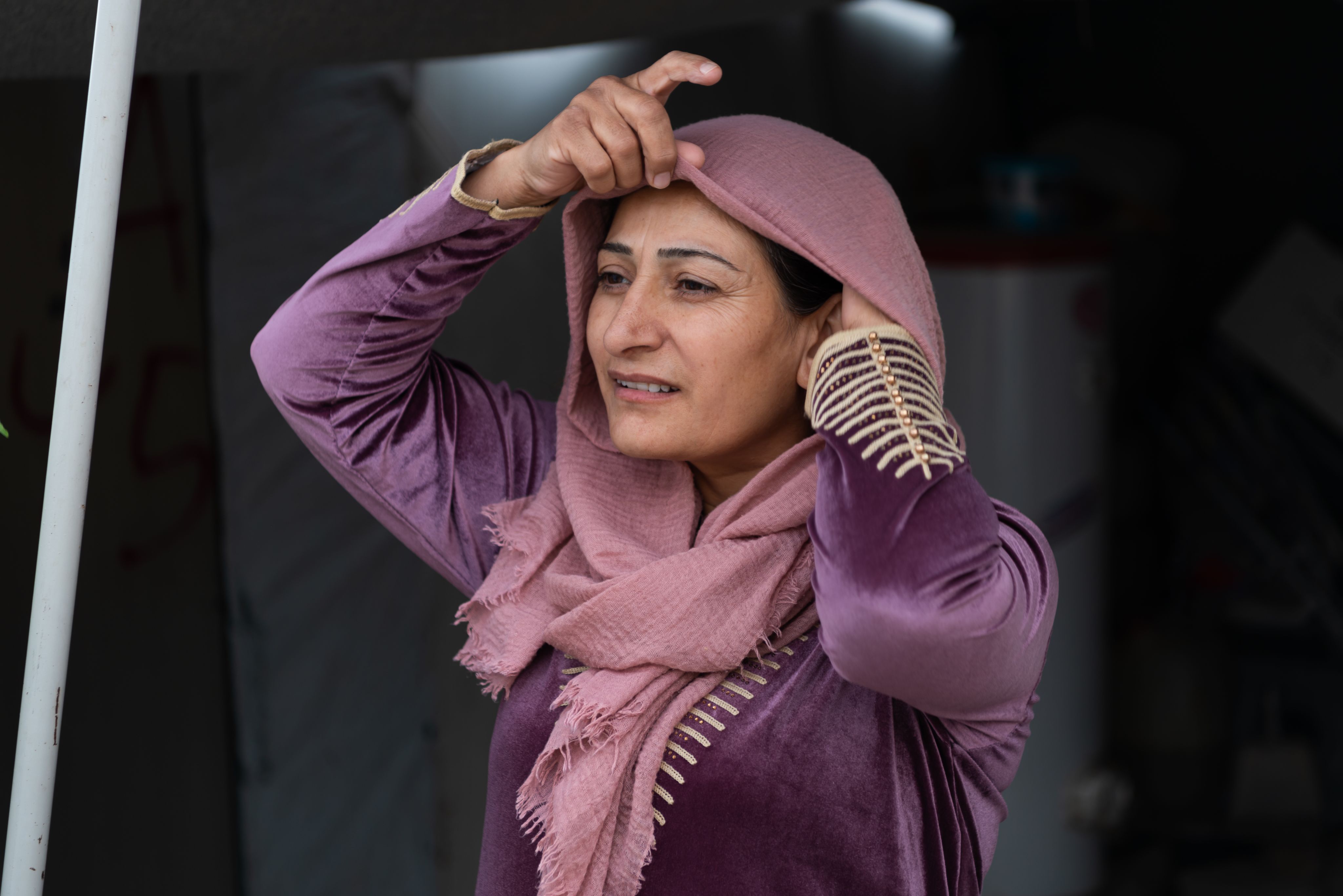 Wwoman lifts her headscarf and stares into distance.