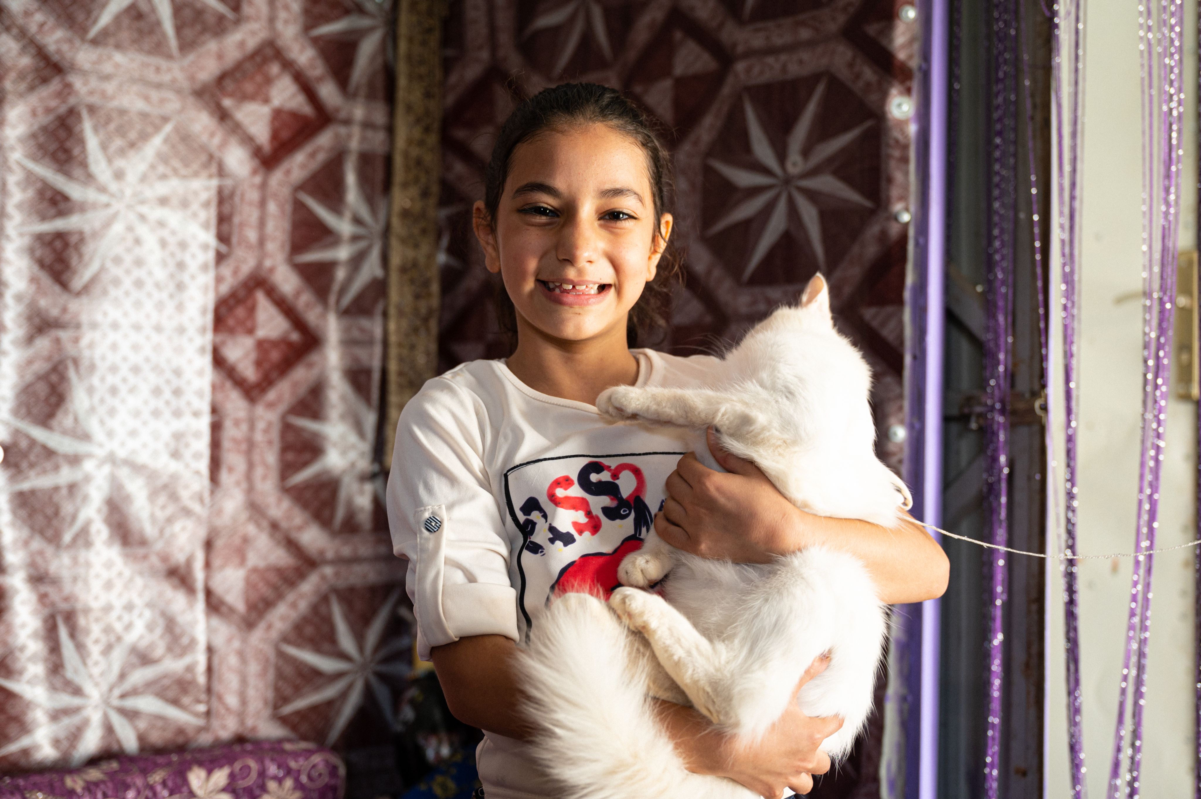 A young Syrian refugee girl holds her cat