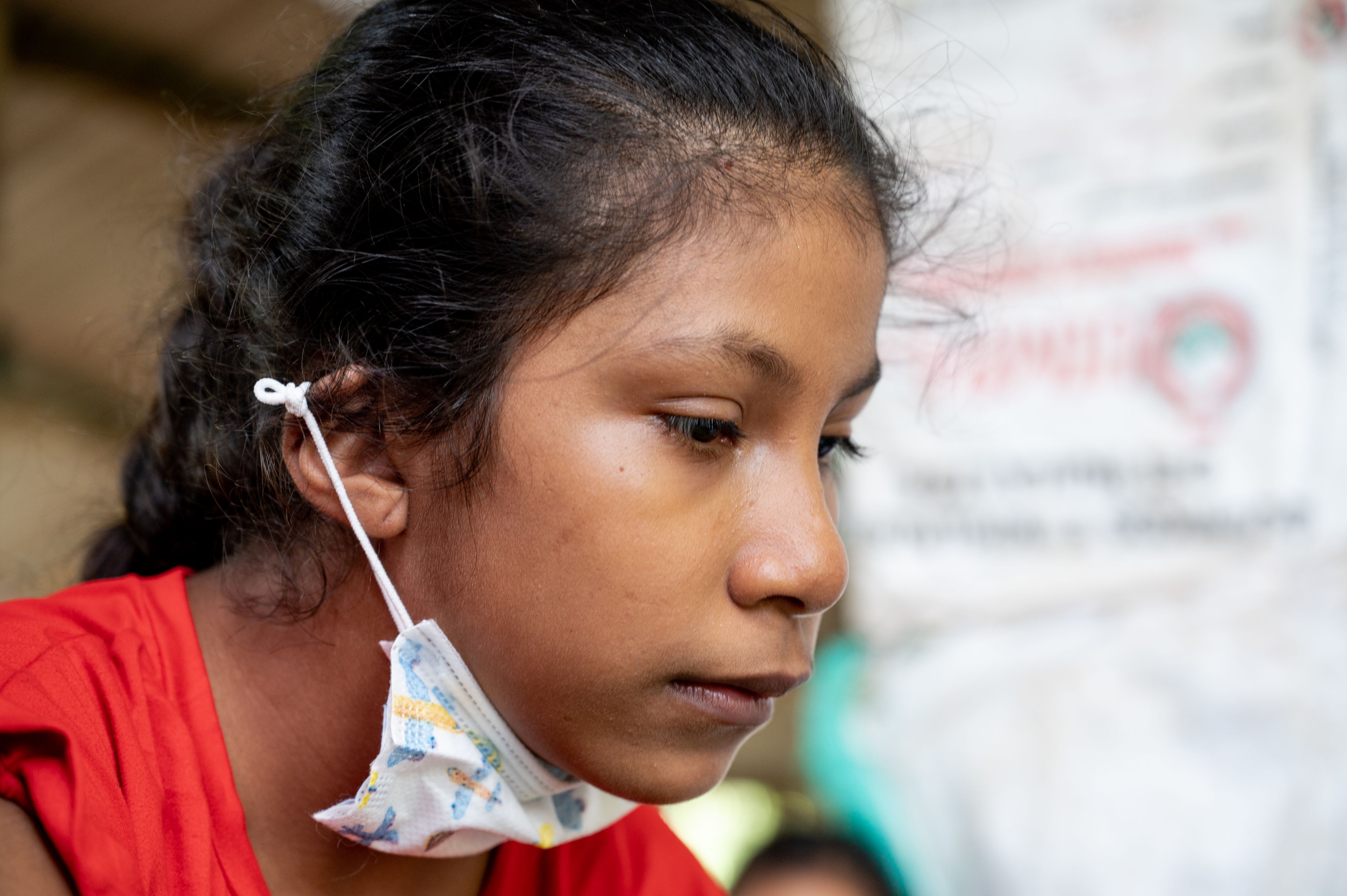 Portrait of a young girl looking down. Her black hair is braided and she has a face mask pulled under her chin.