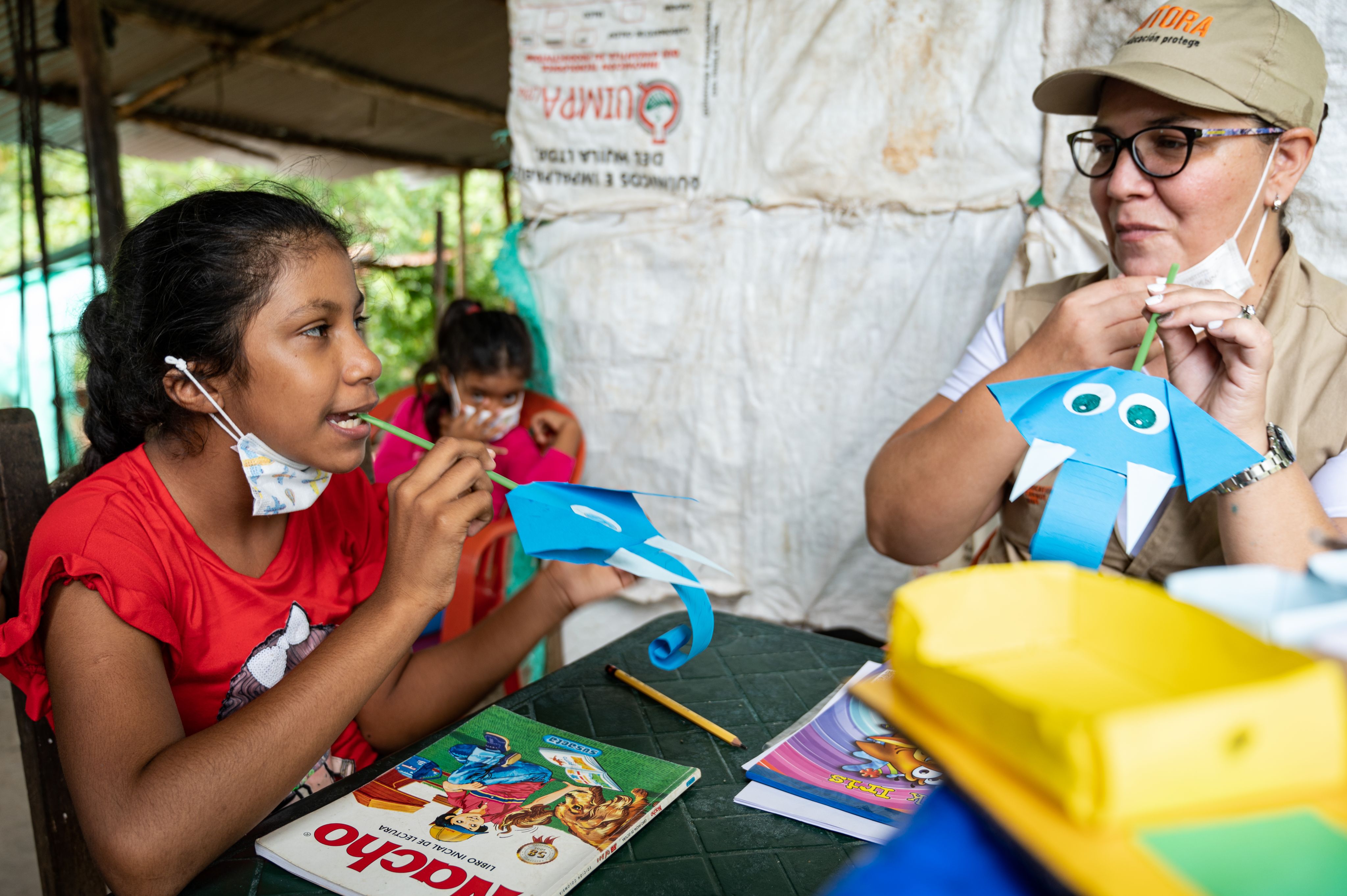 A young girl and her tutor is playing with blue paper elephants and straws.