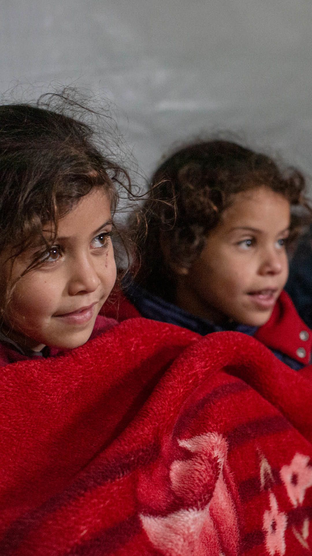 Amira och Aya sitter under en röd filt.