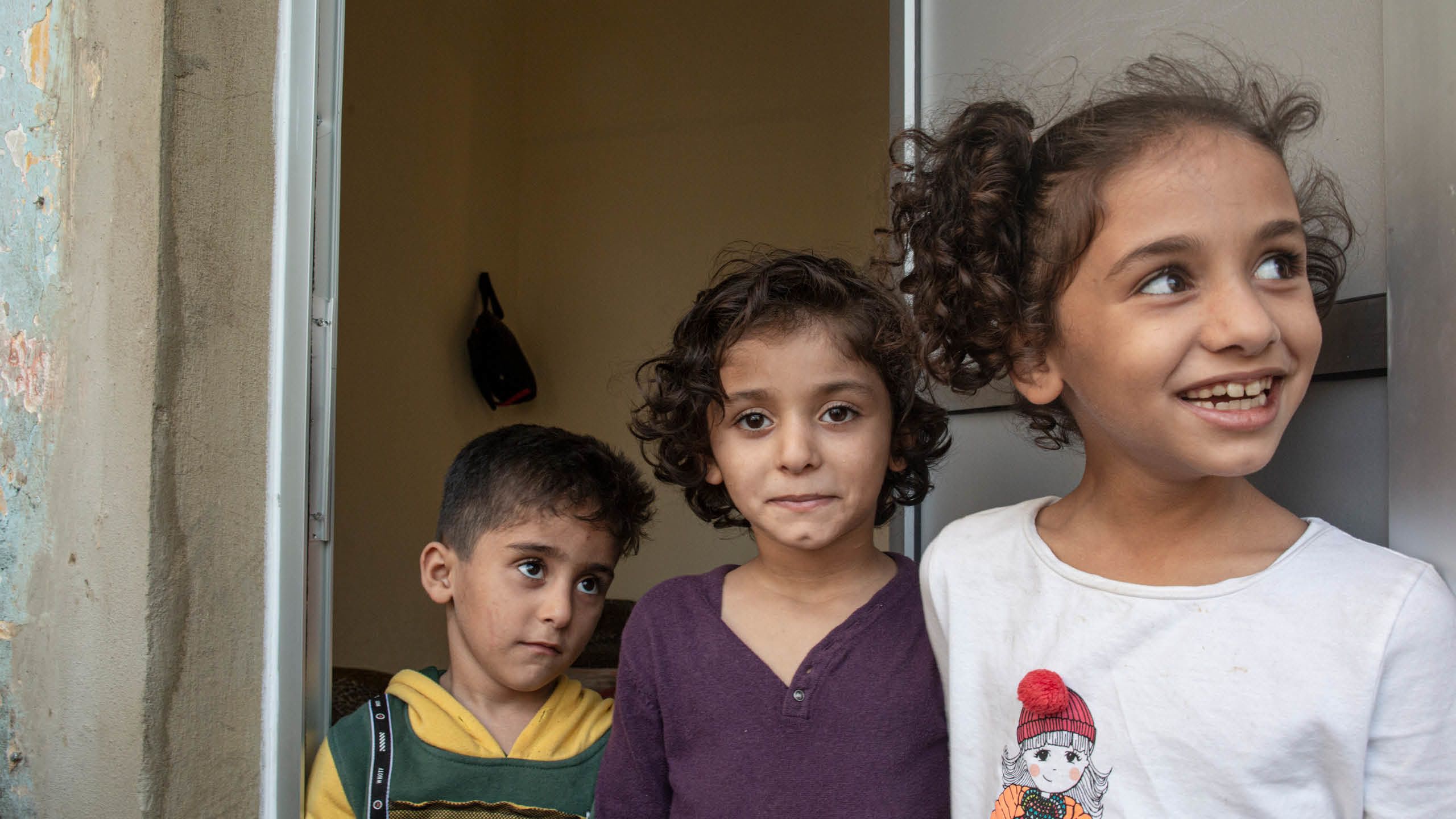 Syskonen Mohammad, 4 år, Jude, 6 år och Fatima, 7 år fotade i dörröppningen till lägenheten.