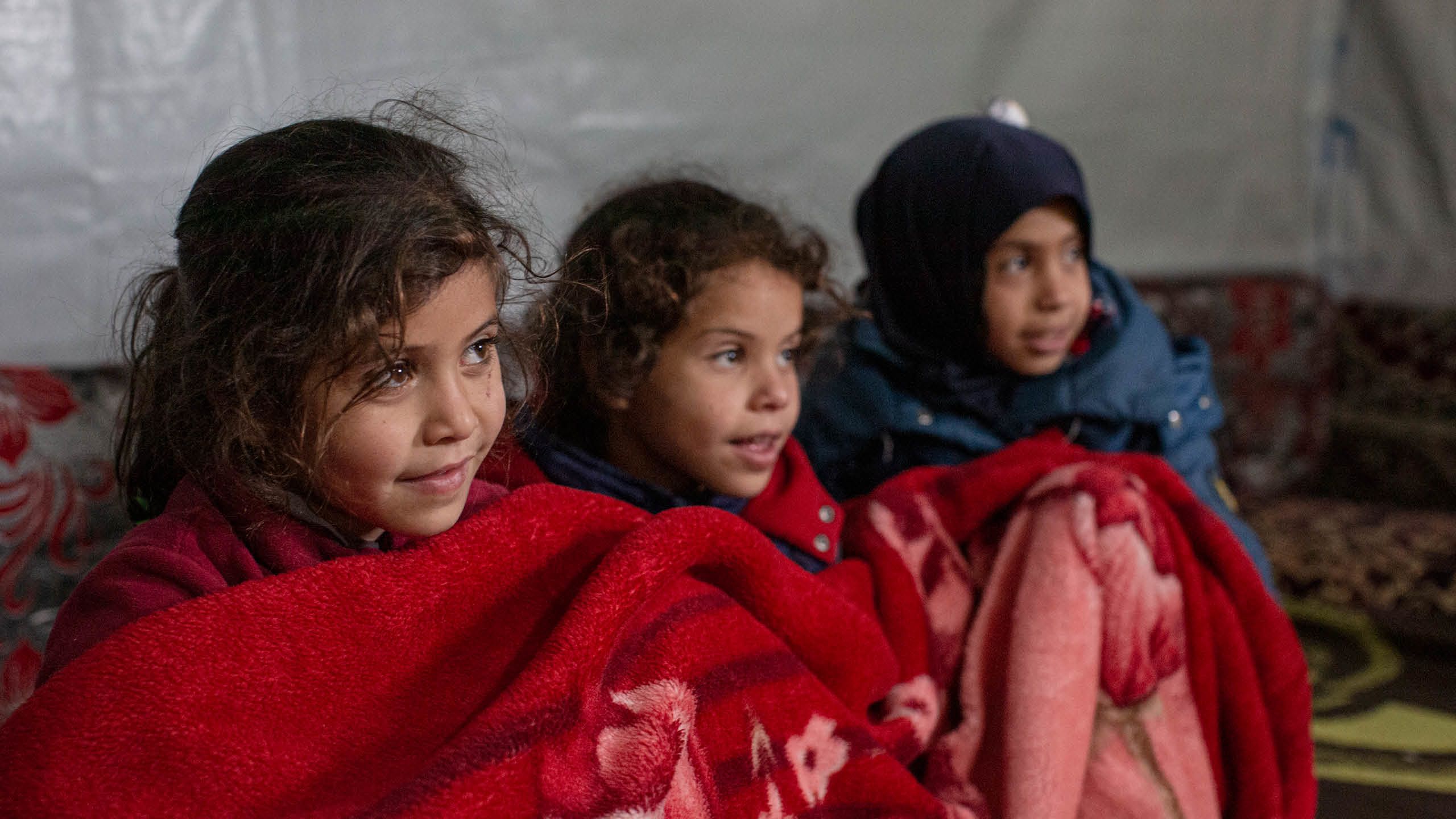 Amira, Aya och Malak Awad sitter under en röd filt.