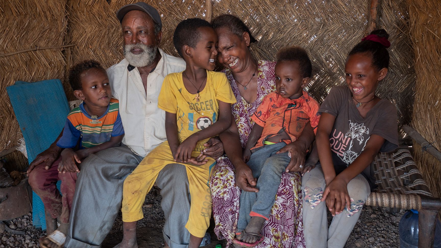 Two grandparents surrounded by four grandchildren. They are holding around each other and laughing.