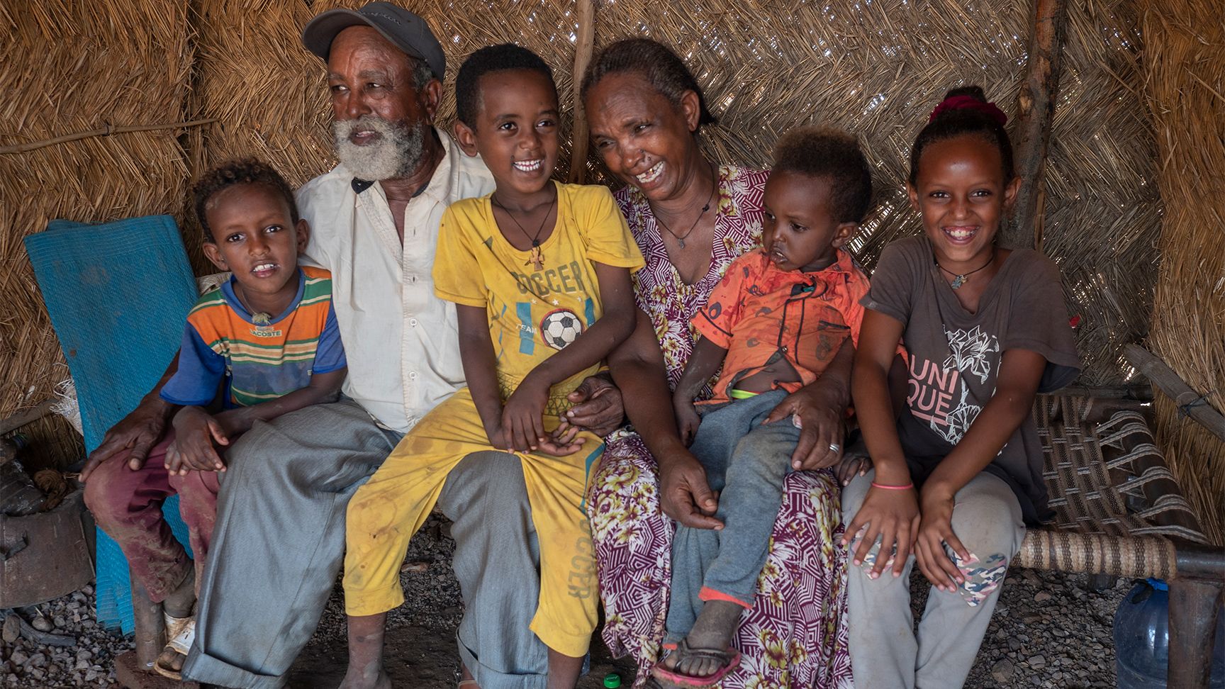 Two grandparents surrounded by four grandchildren. They are holding around each other and laughing.