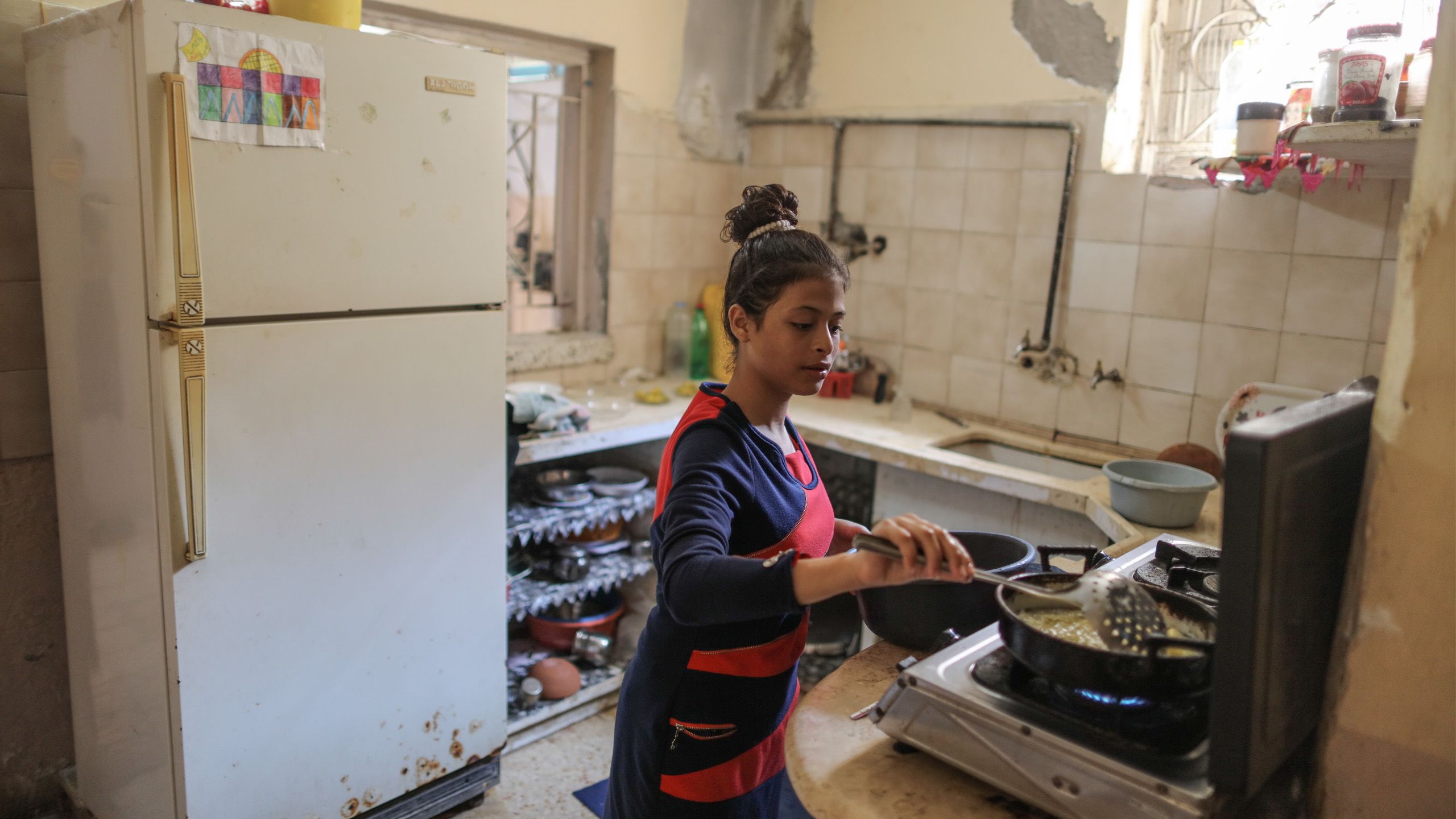 Omaia, at 13 years old, is standing in the kitchen, cooking for her family.