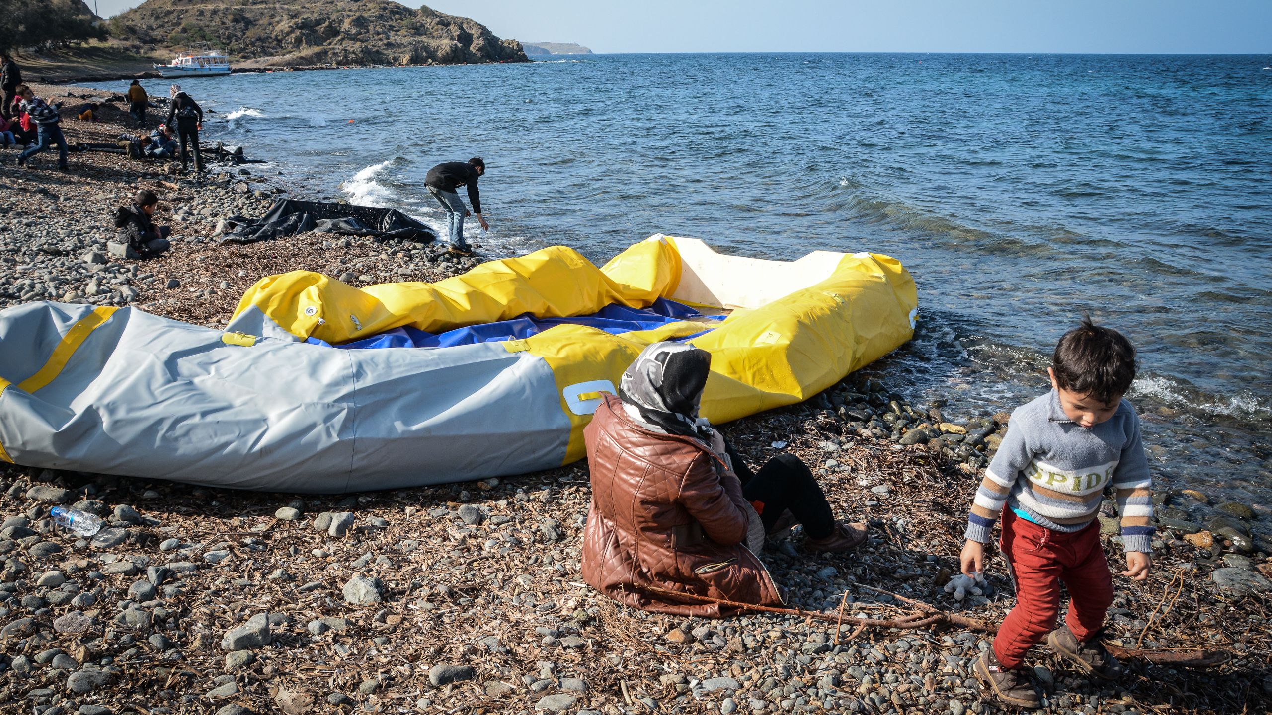A woman sitting on the beach next to a large, deflated rubber boat.